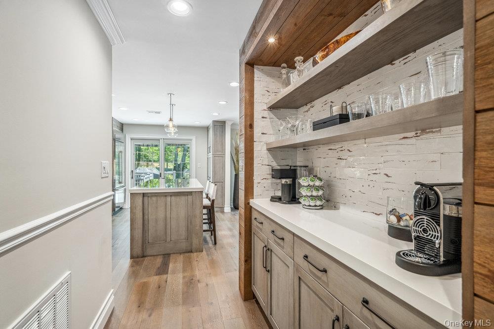 Built-in beverage station featuring open shelving, white countertop, and light wood-finish cabinetry