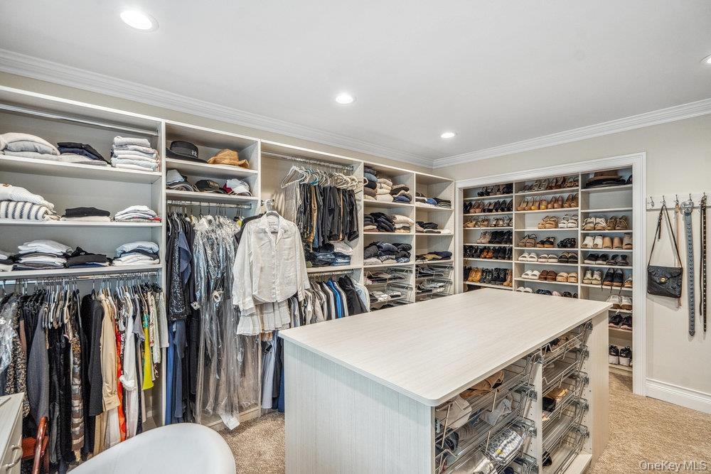 Custom built-in shelving, recessed lighting, crown molding, a central island with storage, and carpeted flooring