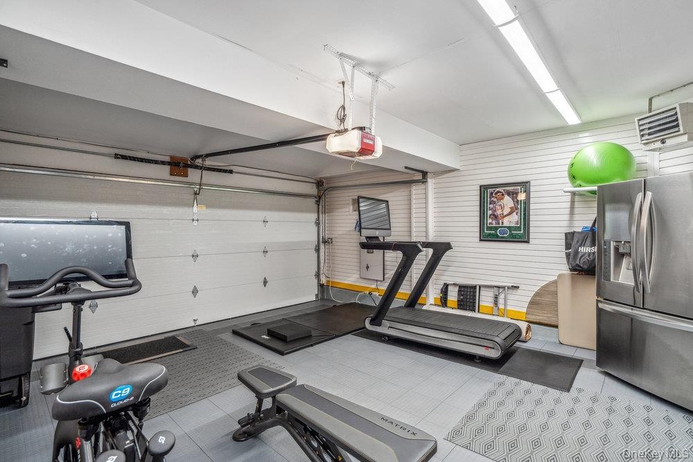Garage featuring a paneled overhead door, white slat wall, durable tile flooring, and integrated overhead lighting