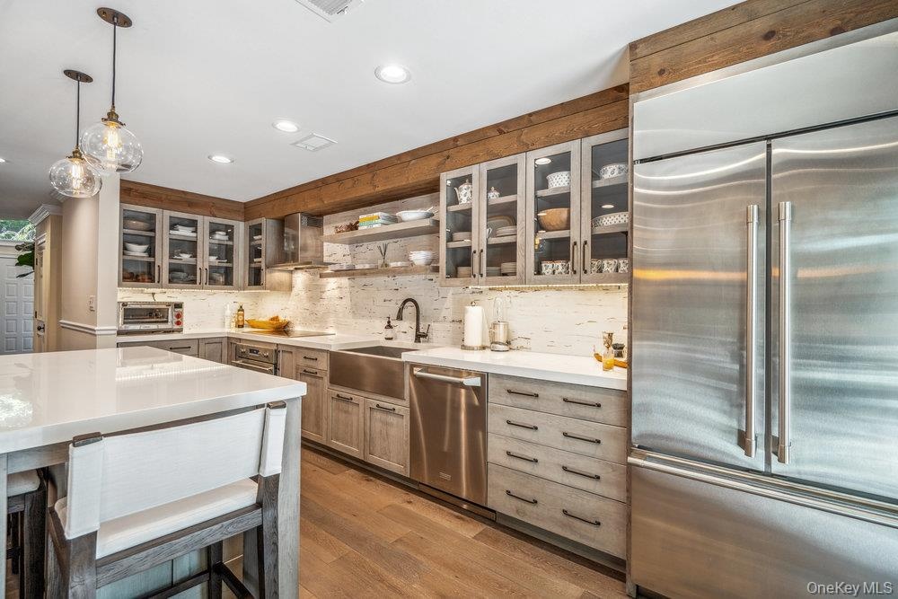 Stainless steel appliances, wood-finish flooring, white countertops, textured backsplash, and glass-front cabinetry