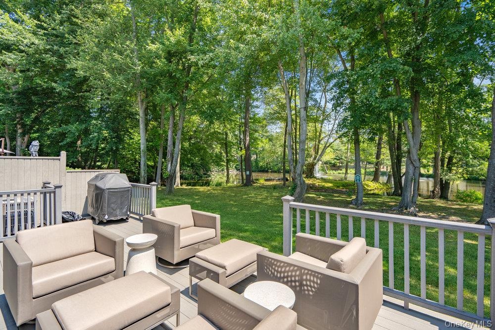 Expansive wood-finish deck with railing overlooking a lush lawn and mature trees