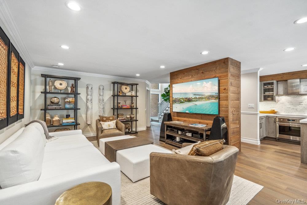 Wood-finish flooring, recessed lighting, built-in shelving, wood accent wall, and a kitchen with stainless steel appliances