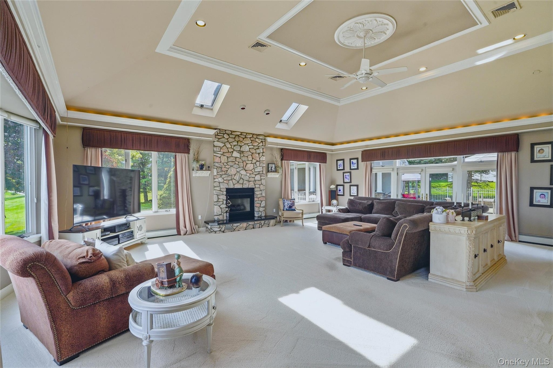 Vaulted ceiling with decorative medallion and ceiling fan, skylights, stone-clad fireplace, and expansive windows