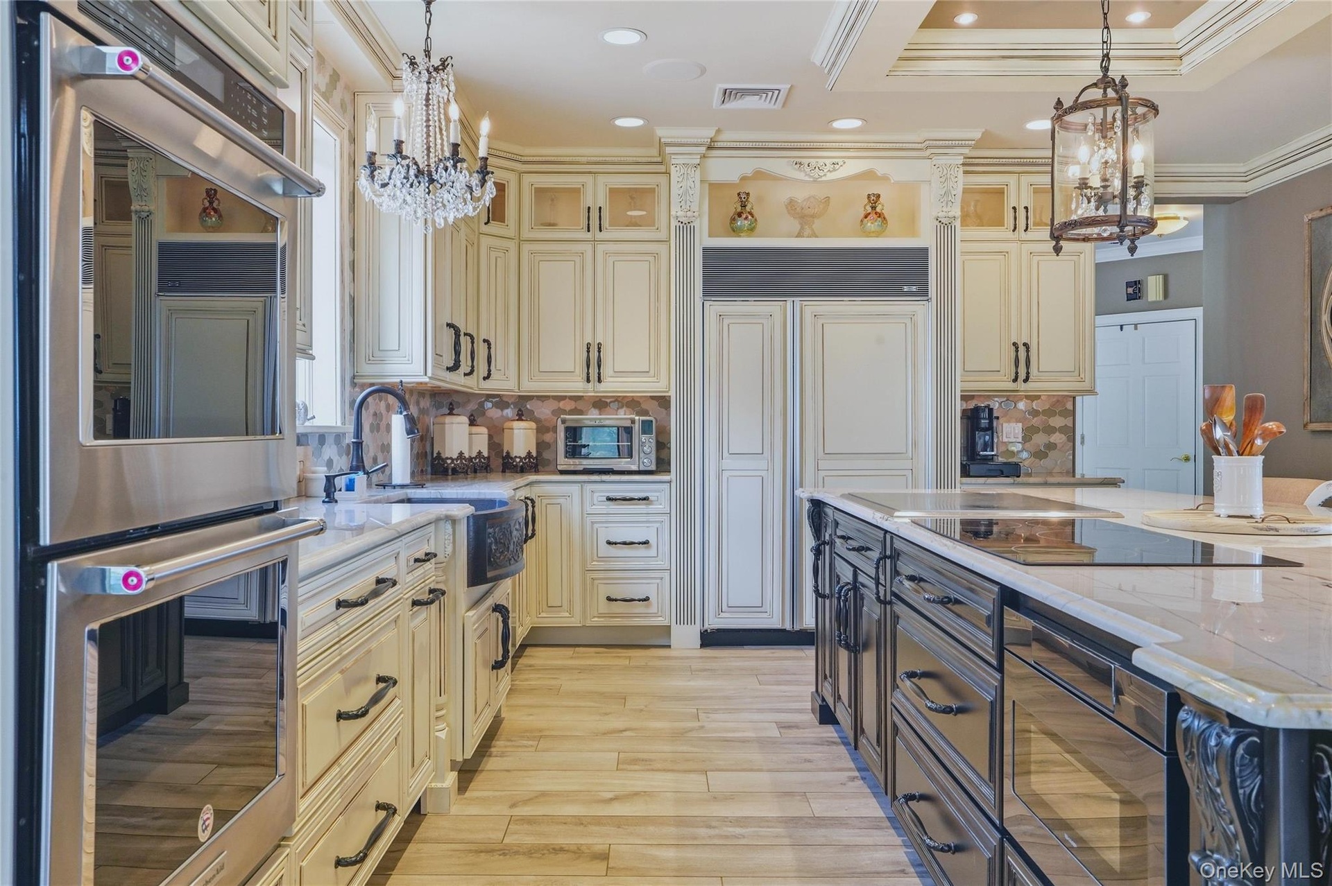 Gourmet kitchen with double wall ovens, integrated refrigerator, custom cabinetry, large kitchen island with cooktop, quartzite counter tops, and wood