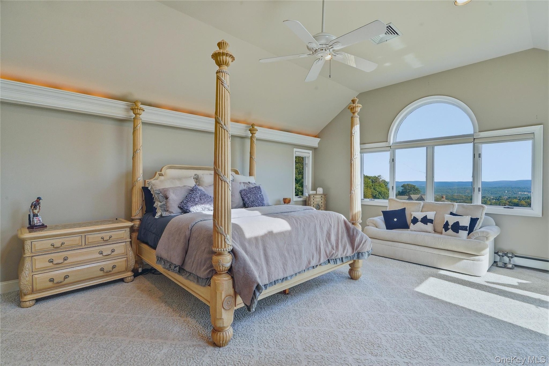 Vaulted ceiling with an overhead fan, large arched window, and plush patterned carpeting