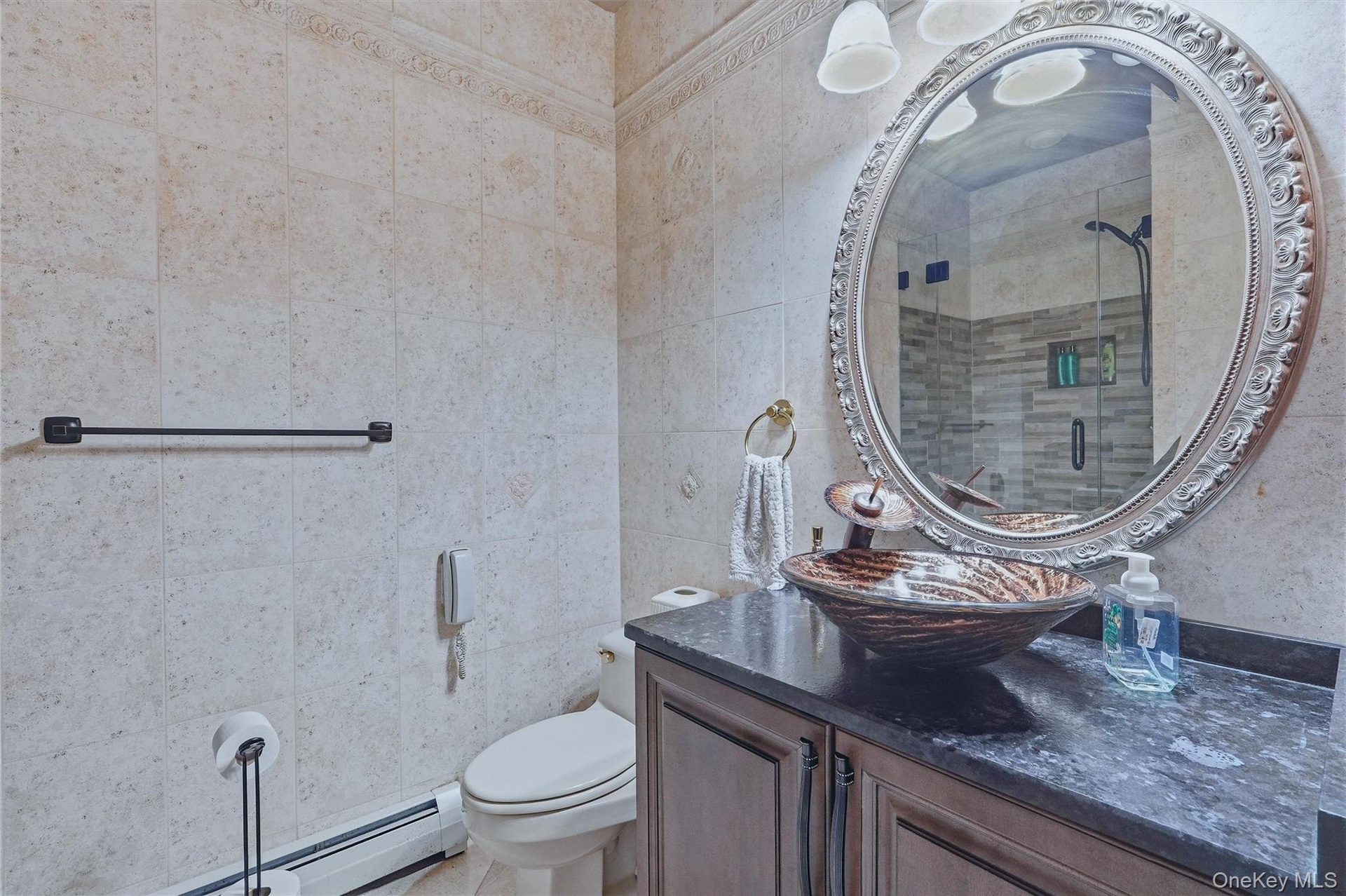 Custom vanity with a dark granite countertop and vessel sink, detailed ornate mirror, and tiled walls with decorative trim