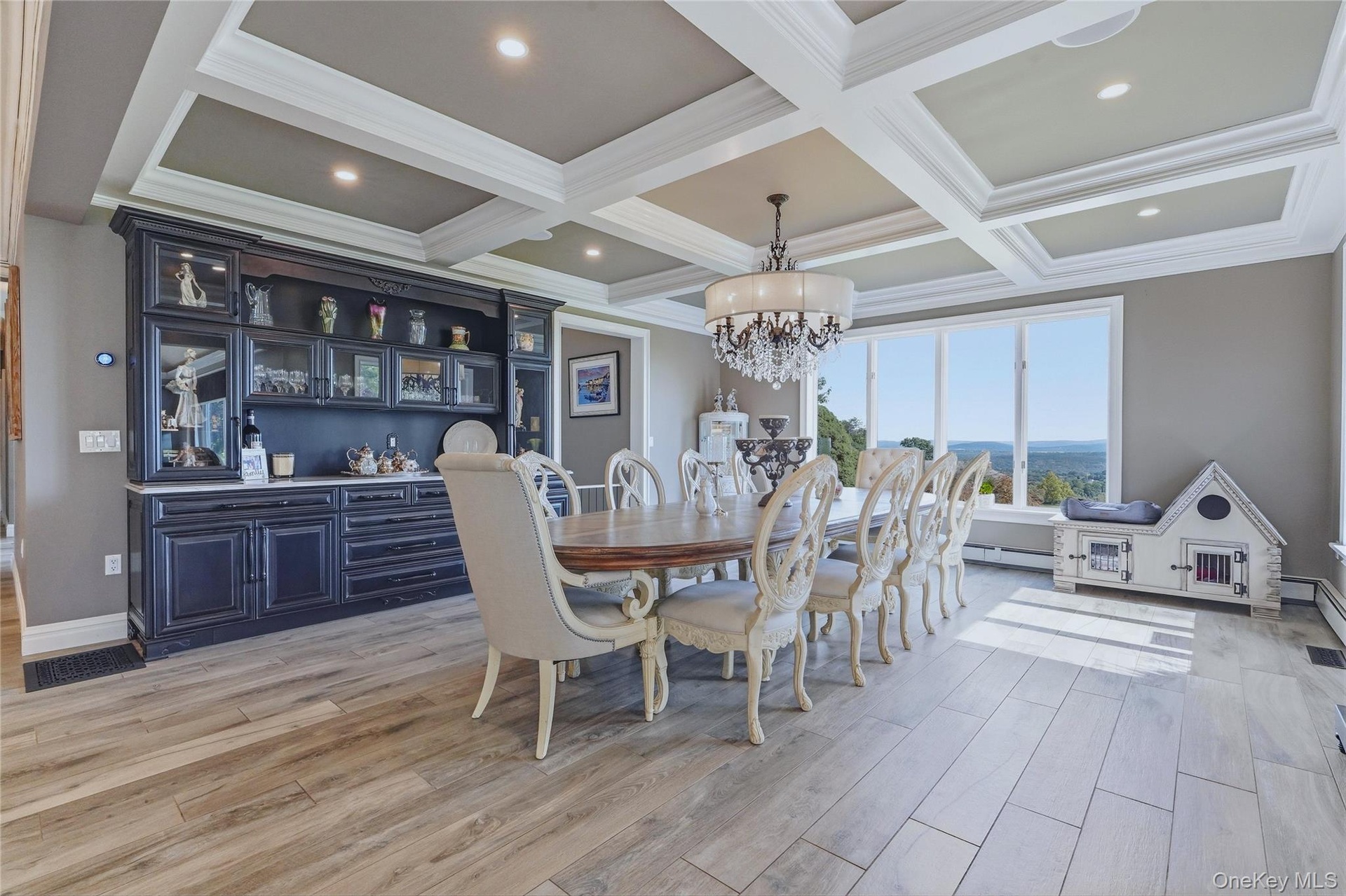 Coffer ceiling with recessed lighting, dark built-in display cabinetry with quartzite counter tops, and large picture windows