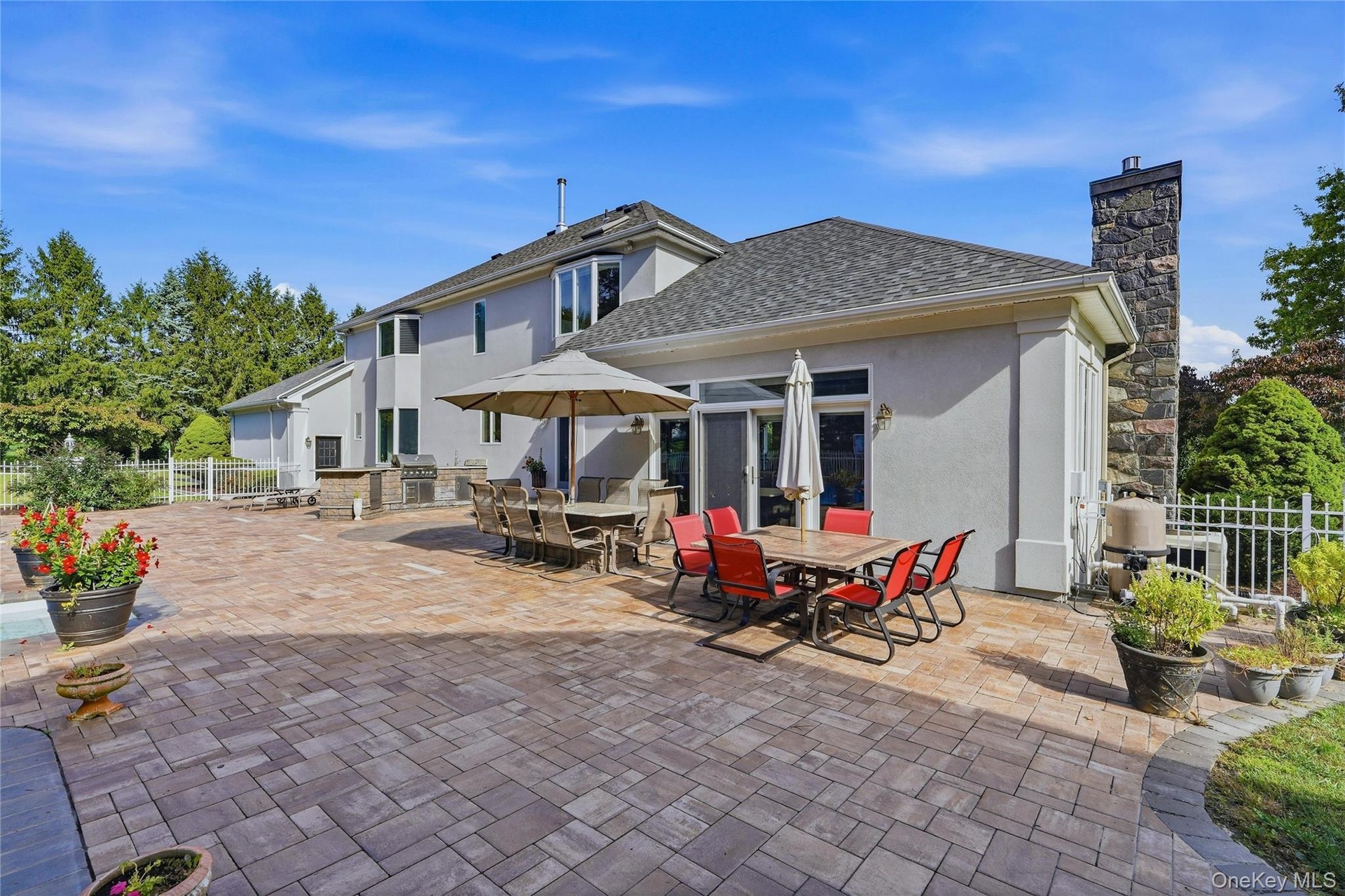 Expansive paver patio with a built-in outdoor kitchen, stone chimney, and stucco exterior