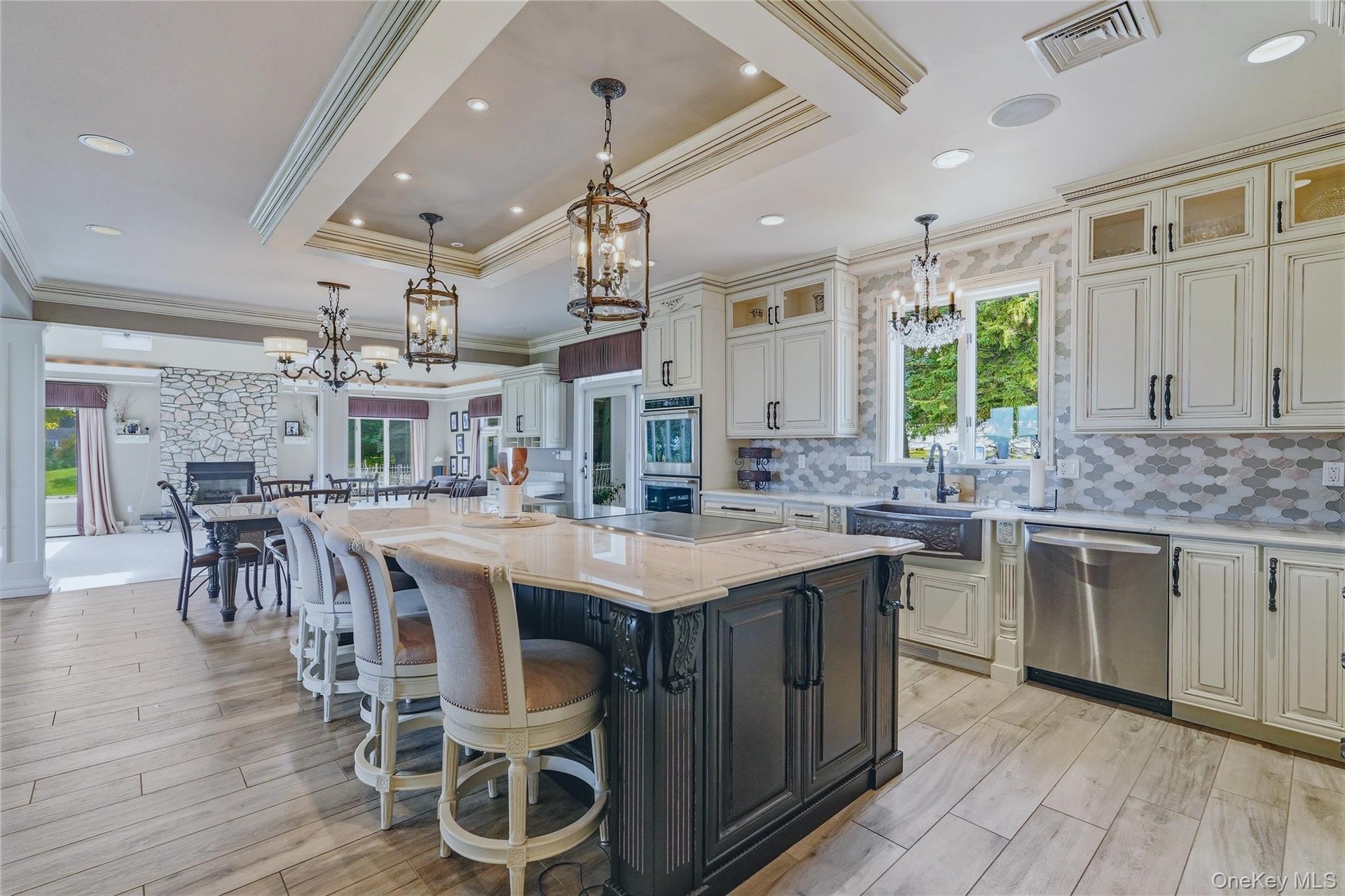 Gourmet kitchen featuring a large central island with seating, white shaker-style cabinetry, stainless steel appliances, and wood-look flooring