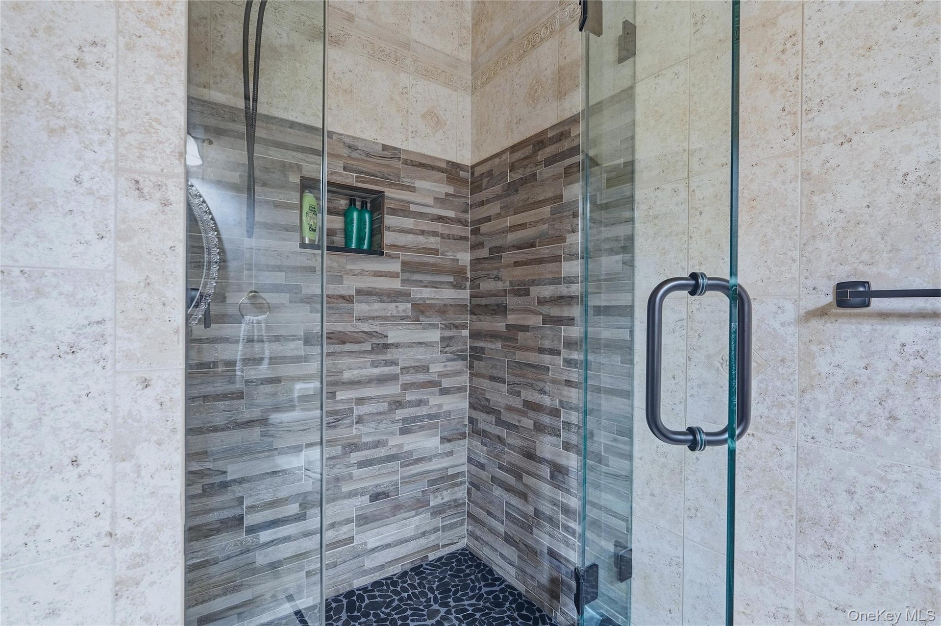Glass-enclosed shower with a river rock floor, tiled walls, and a built-in shower niche