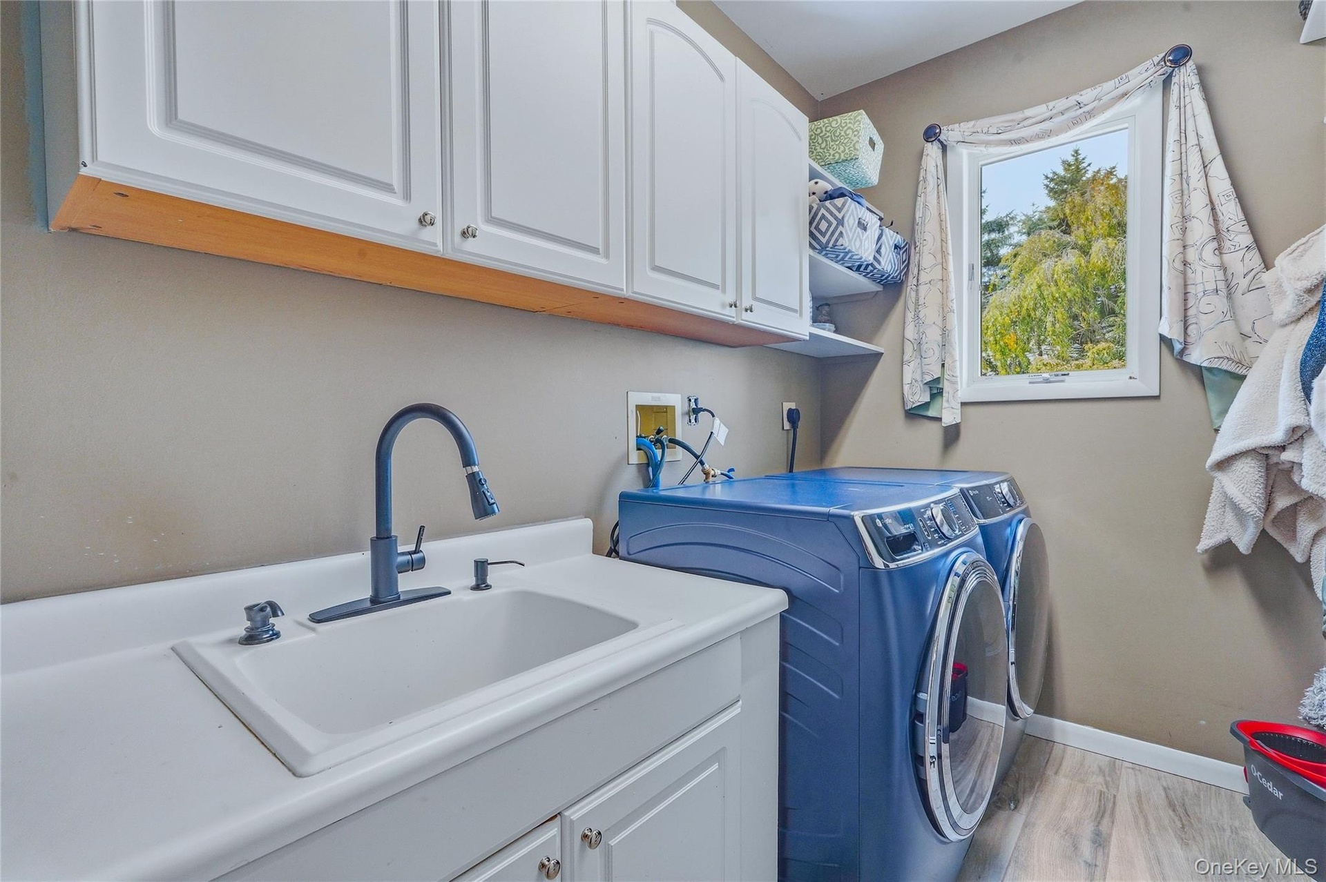 White cabinetry, a utility sink with a matte black faucet, and wood look flooring