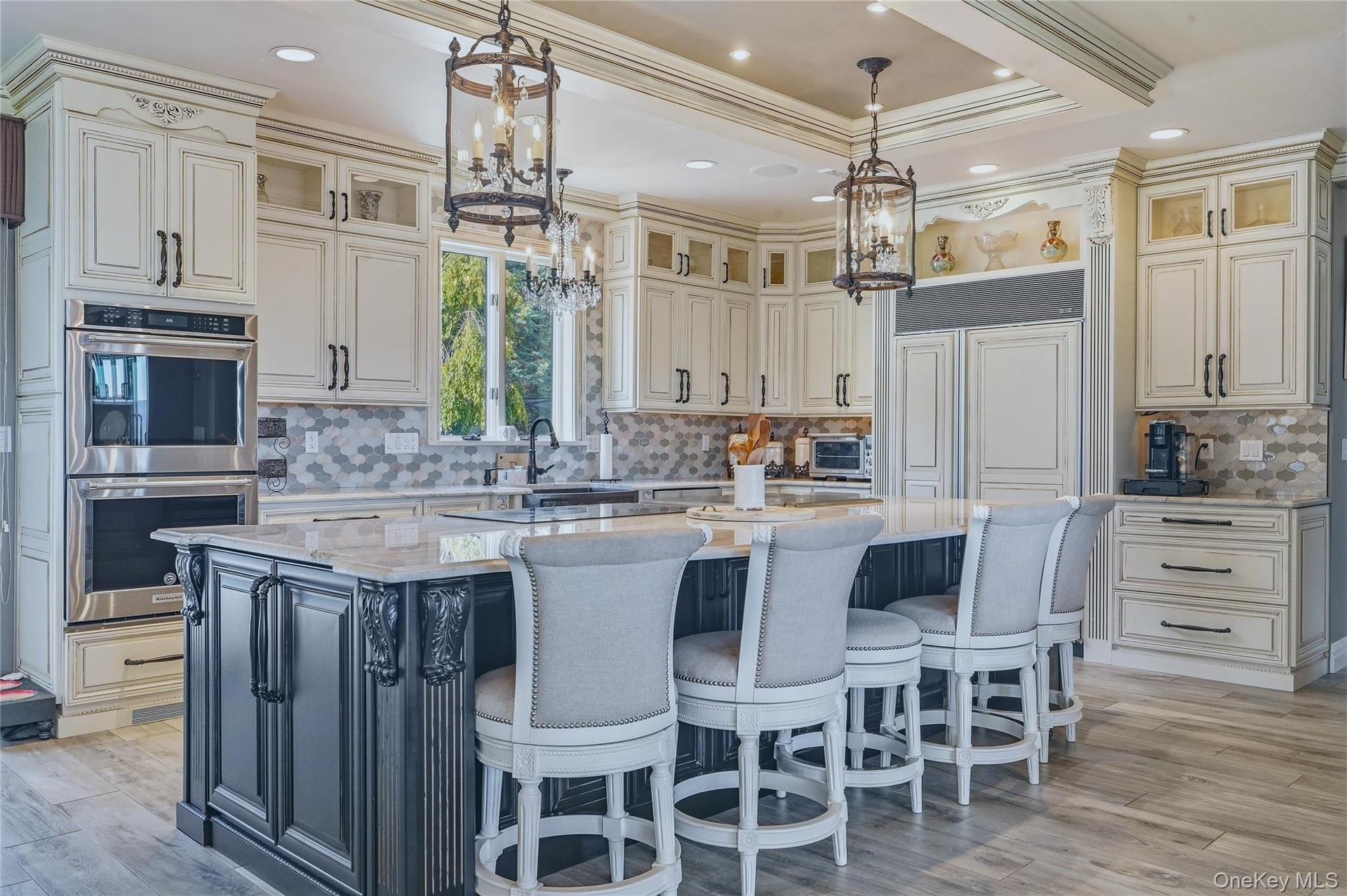 Gourmet kitchen featuring a large central island with seating, stainless steel built-in double ovens, extensive cabinetry, and a patterned marble back
