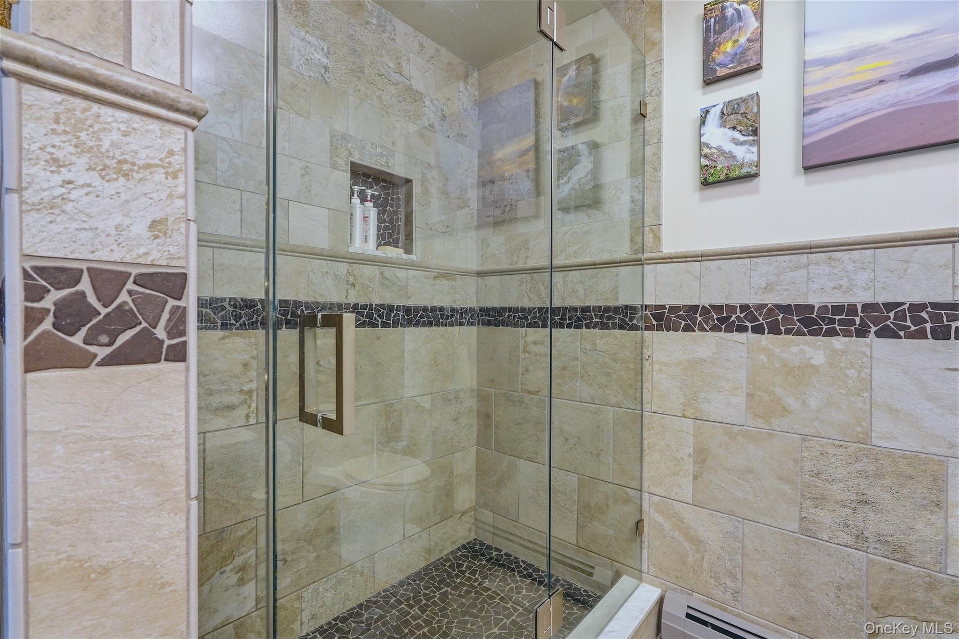 Glass-enclosed shower featuring natural stone-finish wall tile, a decorative mosaic tile band, a recessed shower niche, and a river rock-finish shower