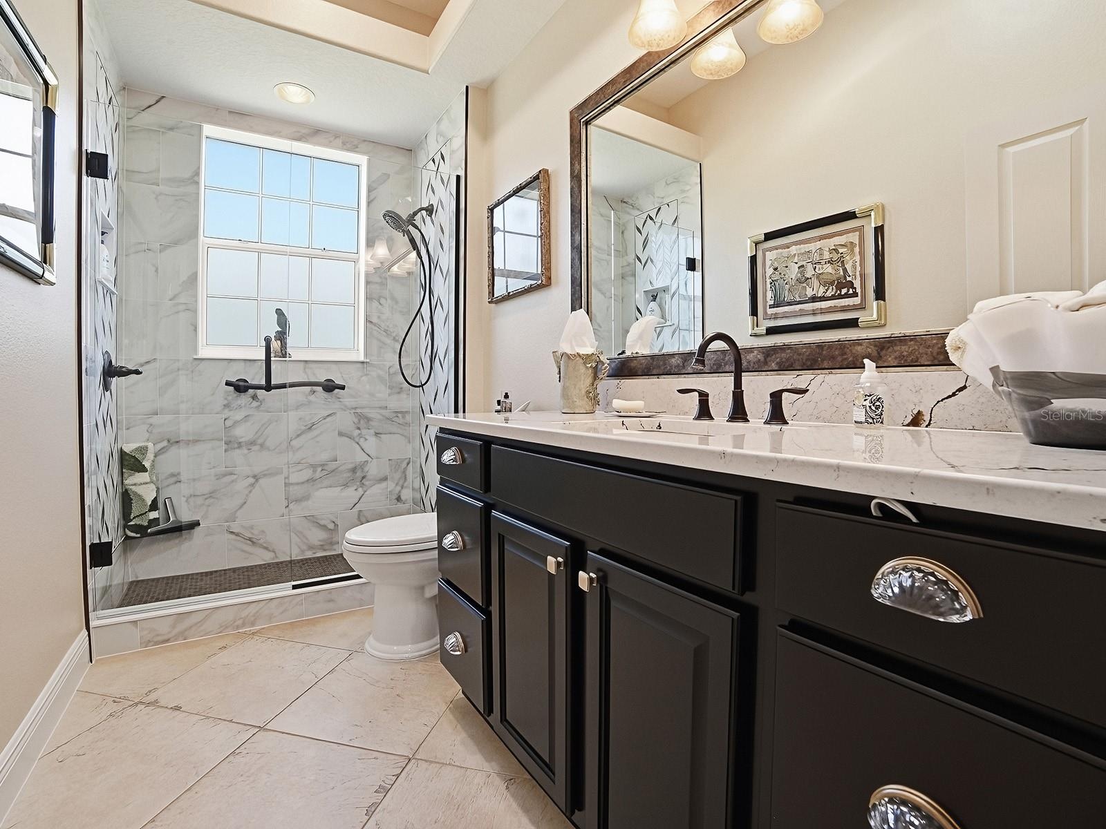 LOVELY RENOVATED GUEST BATH WITH FRAMELESS GLASS DOOR TO THE TILED SHOWER, QUARTZ COUNTERS FRAMED MIRROR AND NEW LIGHT FIXTURE.  ALL OF THE TOILETS IN