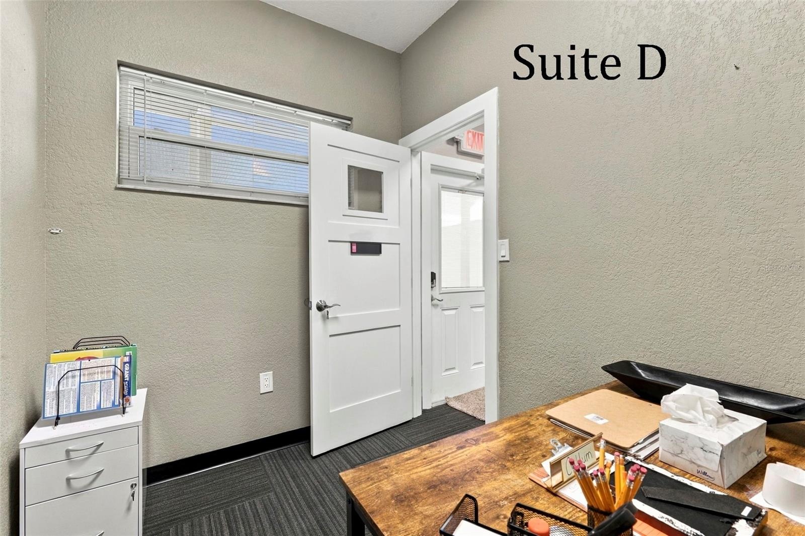 Suite D has a high window and is located near the hall restroom and Covered Patio Break Common Area