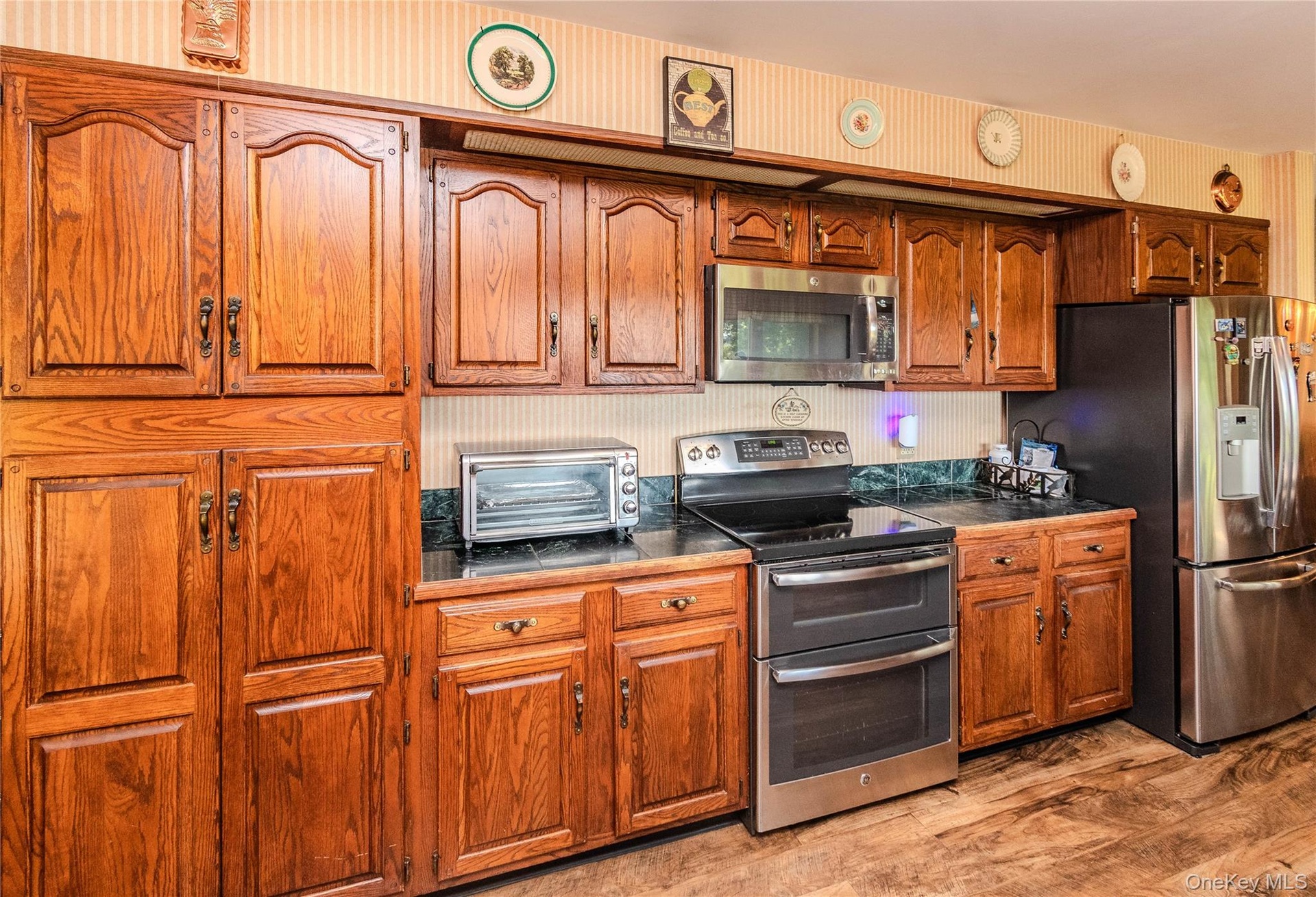 Wood-finish cabinetry with dark hardware, dark countertops, built-in stainless steel microwave, and wood-finish flooring