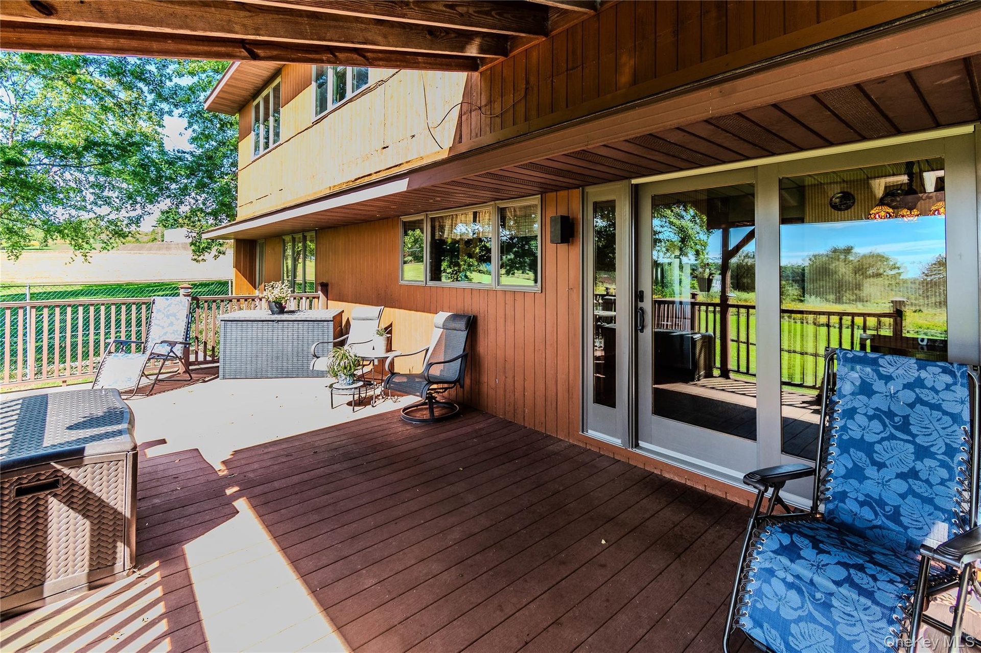 Expansive outdoor deck with wood-finish flooring, sliding glass doors, and a wood-paneled exterior