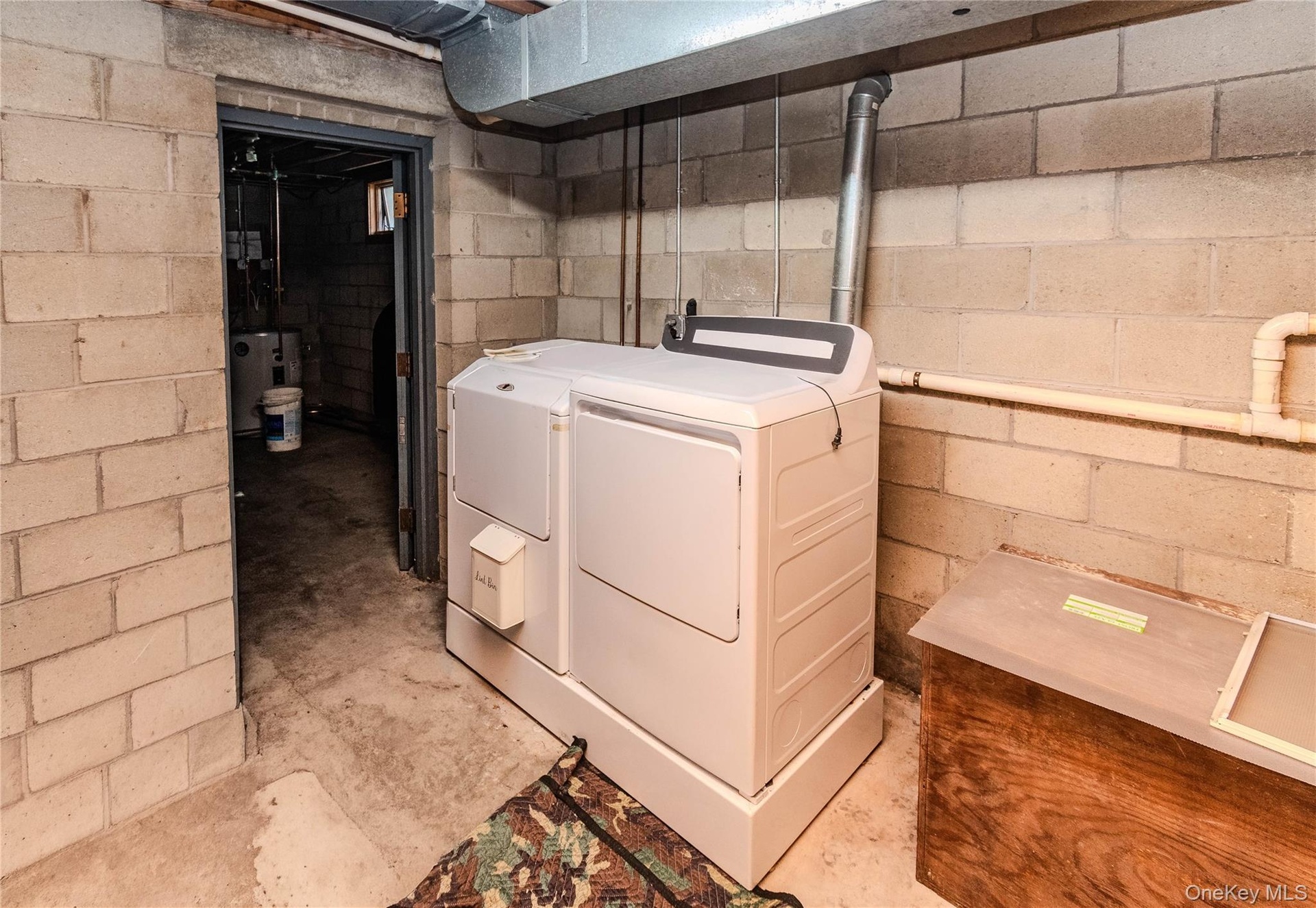 Laundry area featuring a side-by-side washer and dryer, concrete block walls, and exposed utility piping
