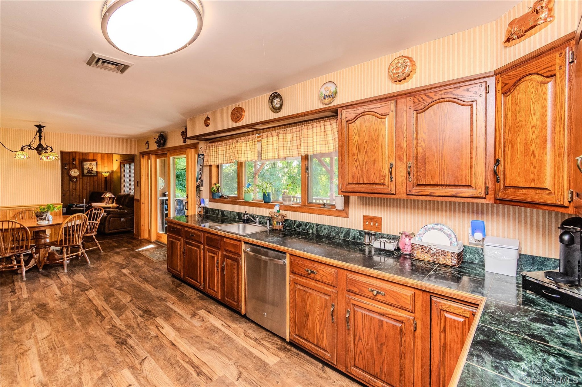Wood-finish flooring throughout, solid wood cabinetry, dark countertops, stainless steel dishwasher, and sliding glass door