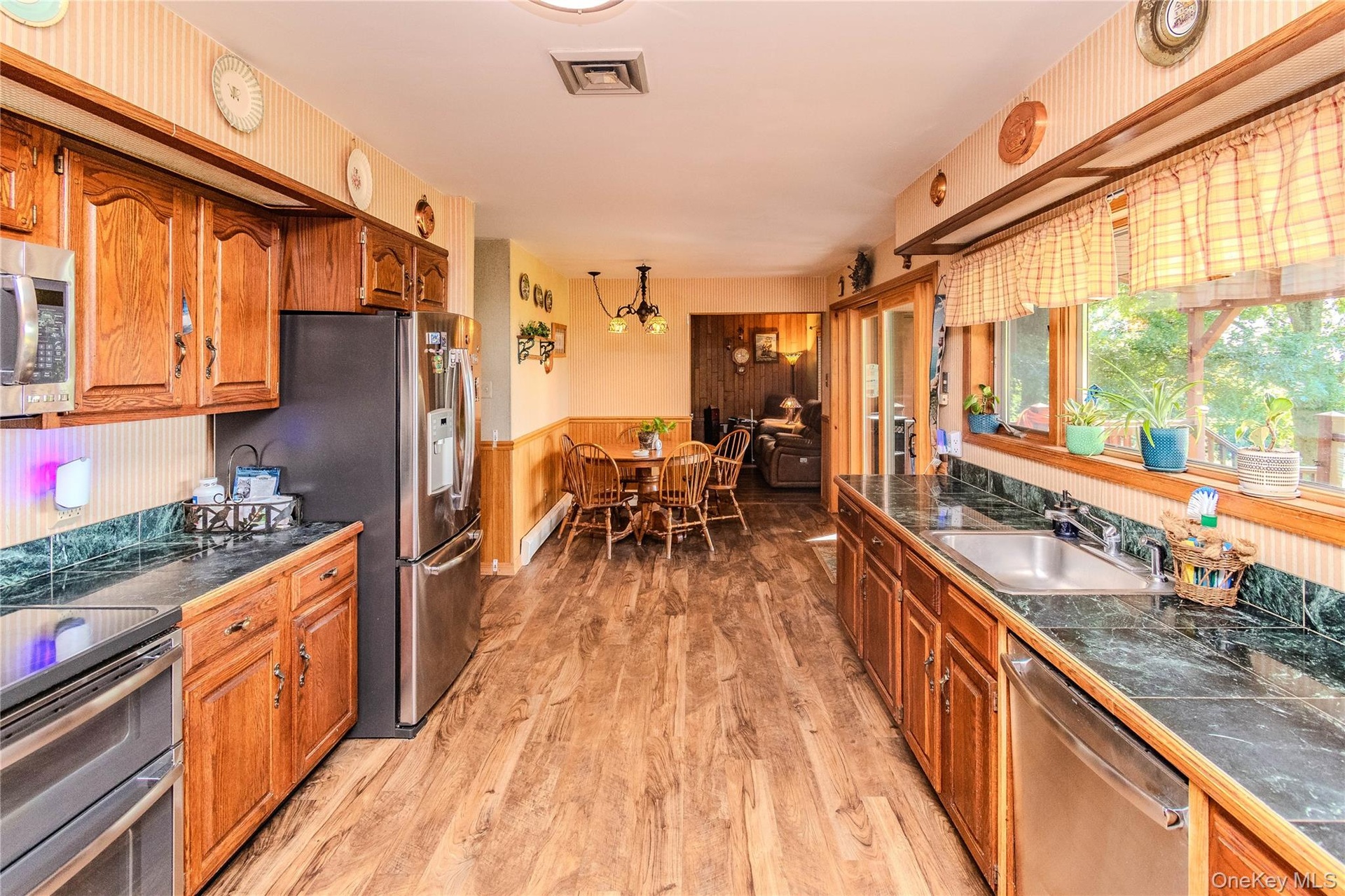Kitchen featuring wood-finish flooring, wood cabinetry, dark countertops, and stainless steel appliances