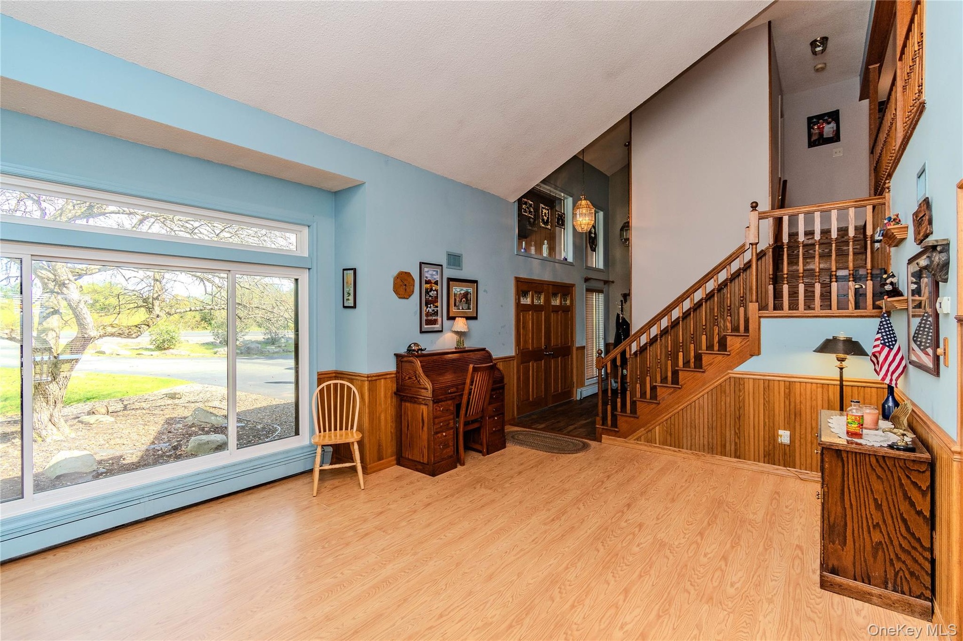 Expansive front window, wood-finish flooring, wood paneling, and a wood staircase with balusters