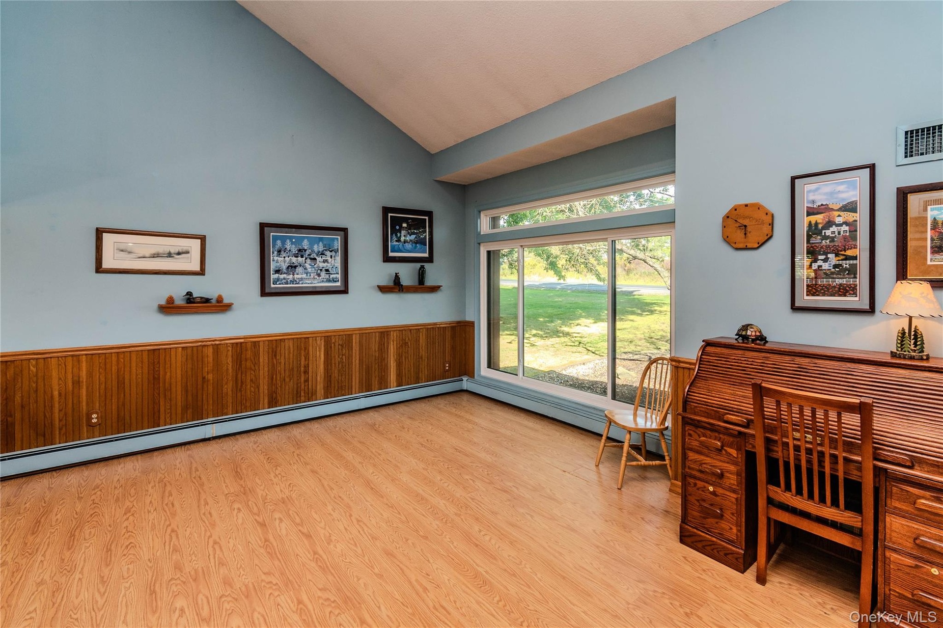Vaulted ceiling, wood-finish flooring, wood paneling, large sliding glass windows, and built-in heat registers