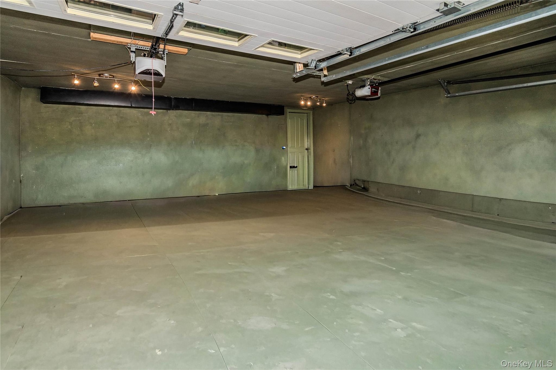 Expansive garage space with concrete flooring, overhead lighting, and two garage door openers