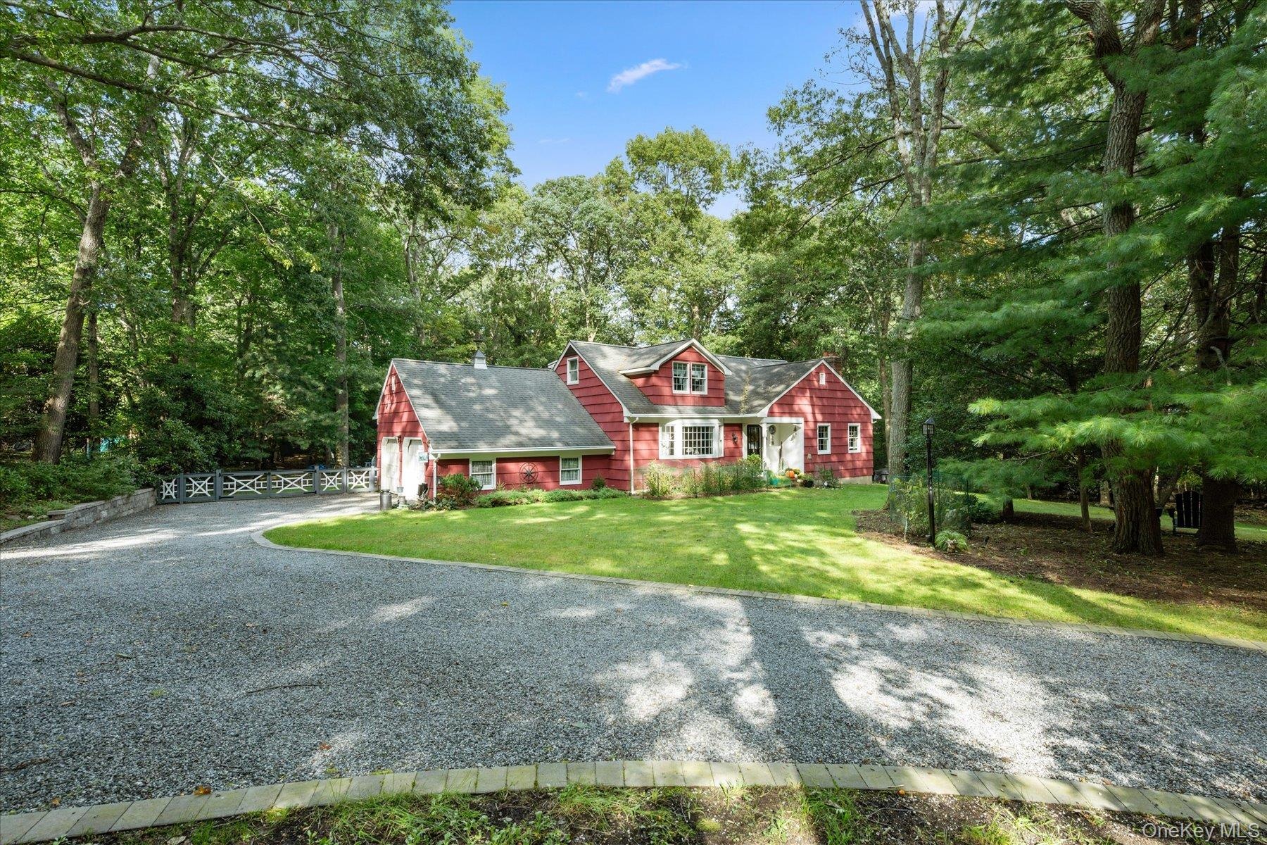 Red siding exterior with white trim, a gravel driveway, and a manicured lawn