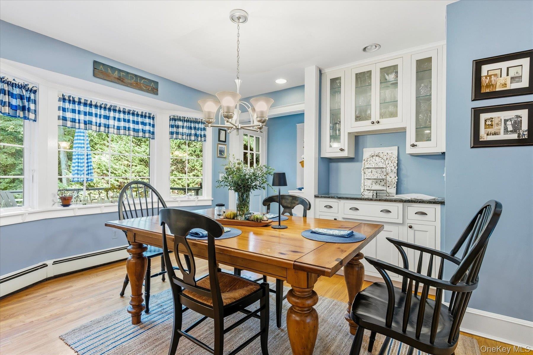 Bay window with multiple panes, wood-finish flooring, white built-in cabinetry with glass panel doors, granite counter