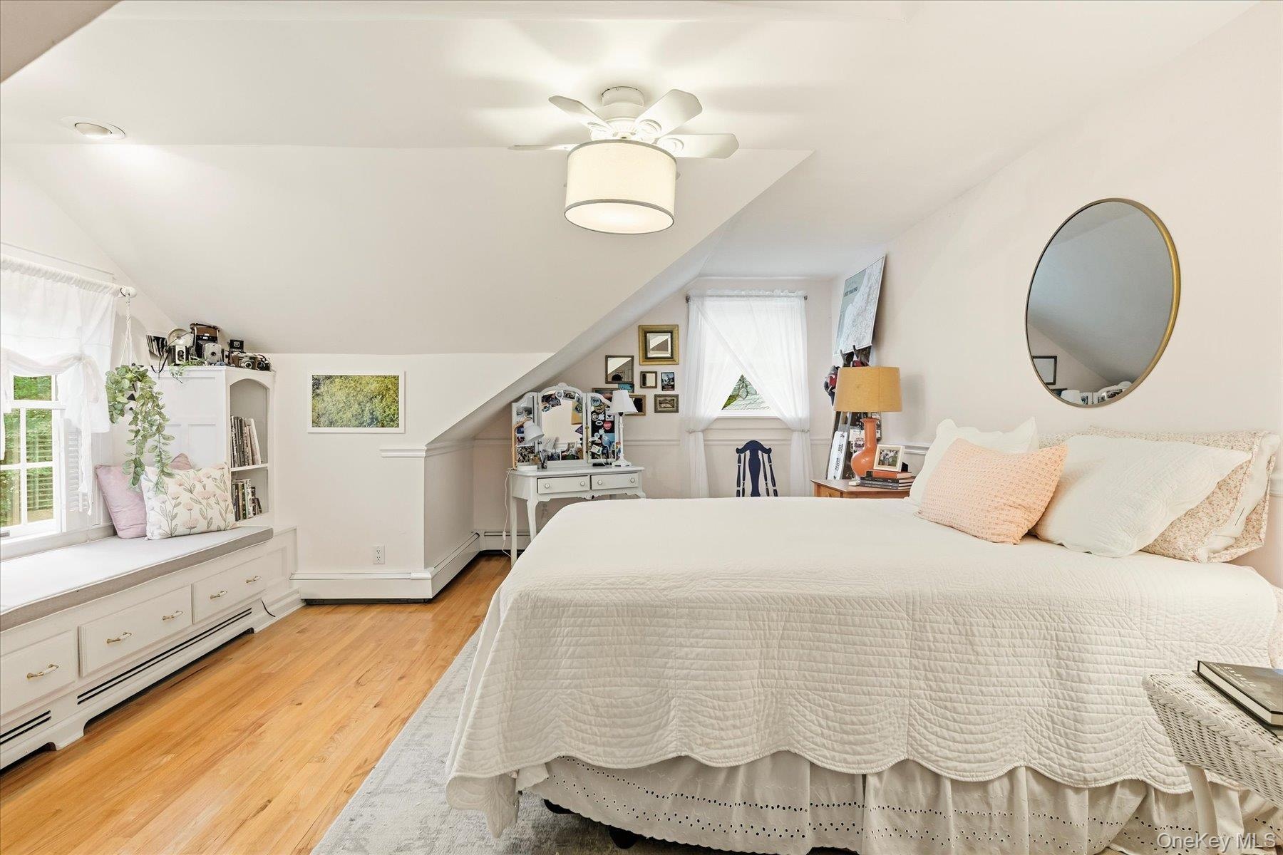 Hardwood flooring, sloped ceiling, built-in window seating with storage, ceiling fan with integrated lighting, and multiple windows
