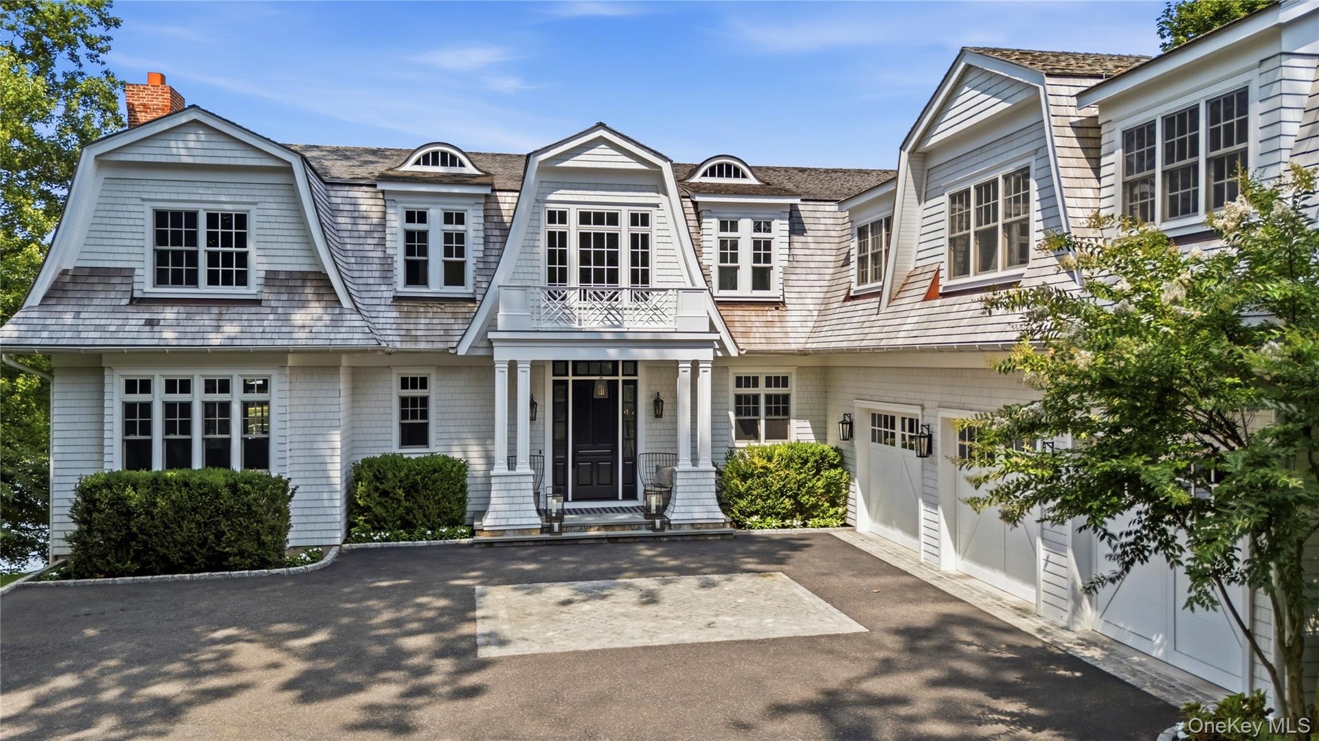 Waterfront home with shingle-style exterior with gambrel roofline, multiple dormers, and an attached three car garage