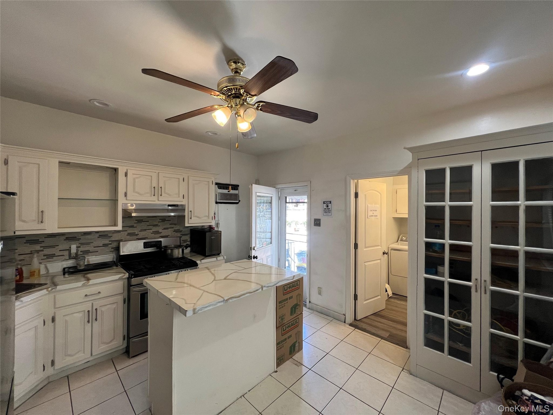 White tile flooring, white cabinetry, stainless steel range with overhead microwave, white island with a light-colored countertop, and a built-in stor