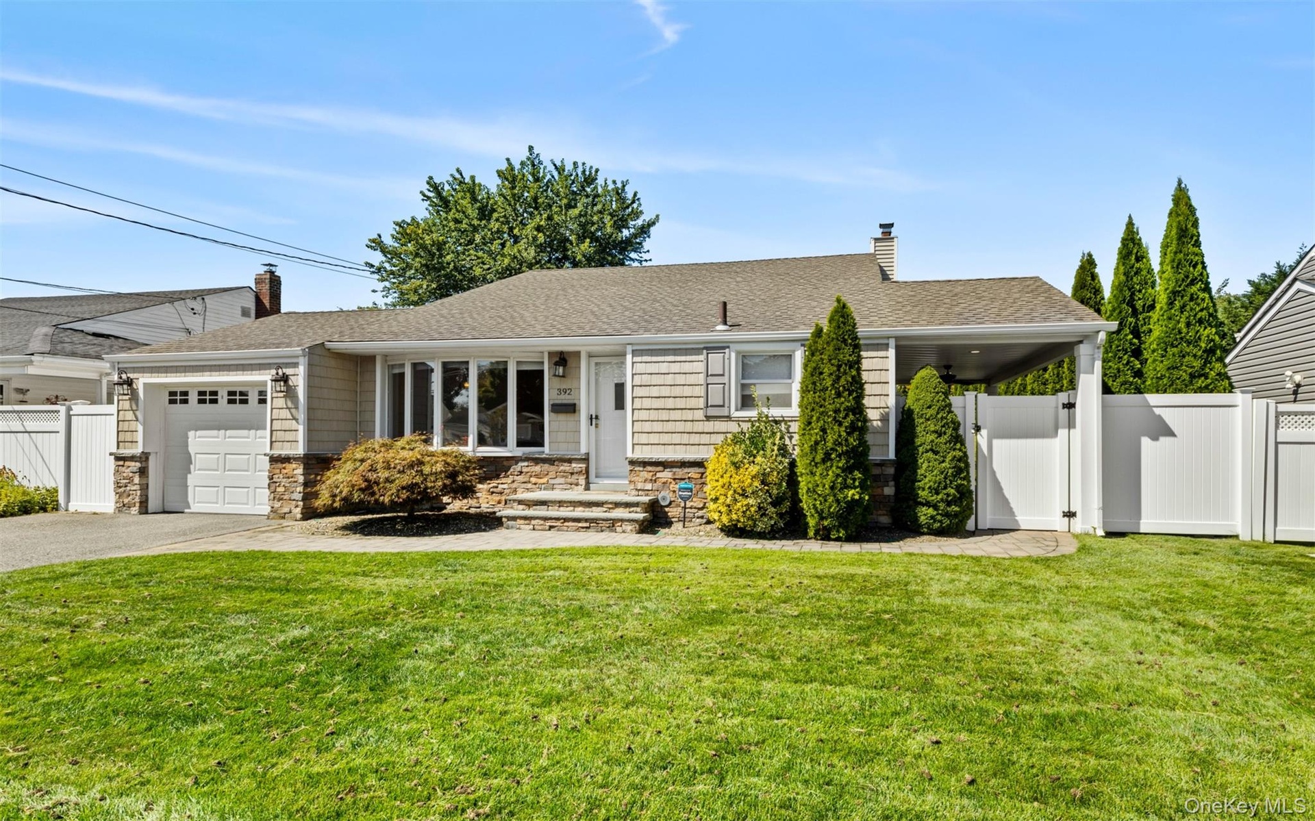 Ranch-style exterior with stone veneer and shingle siding, an attached garage, a covered carport, and a paved driveway