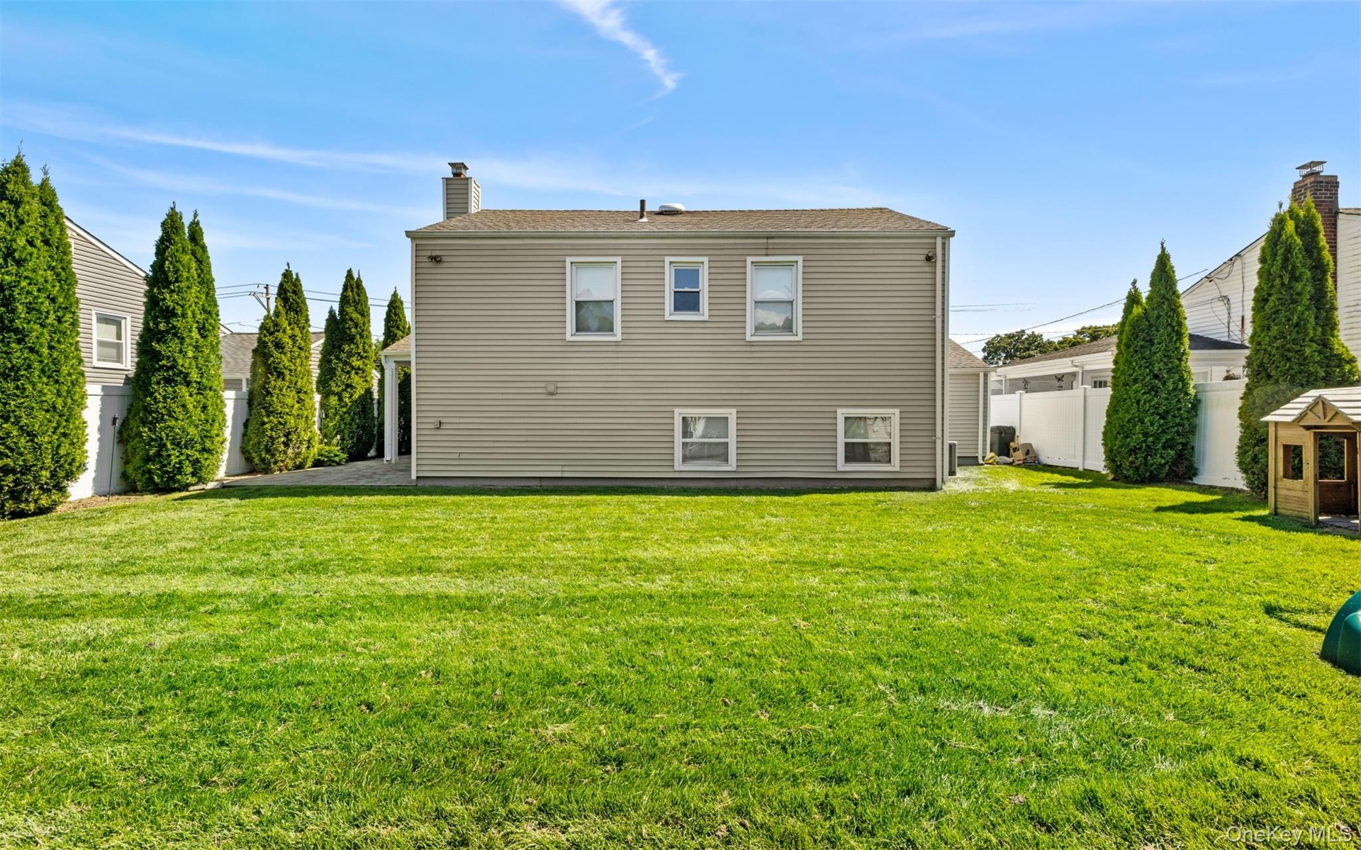 Expansive green lawn with mature evergreen trees and a white privacy fence