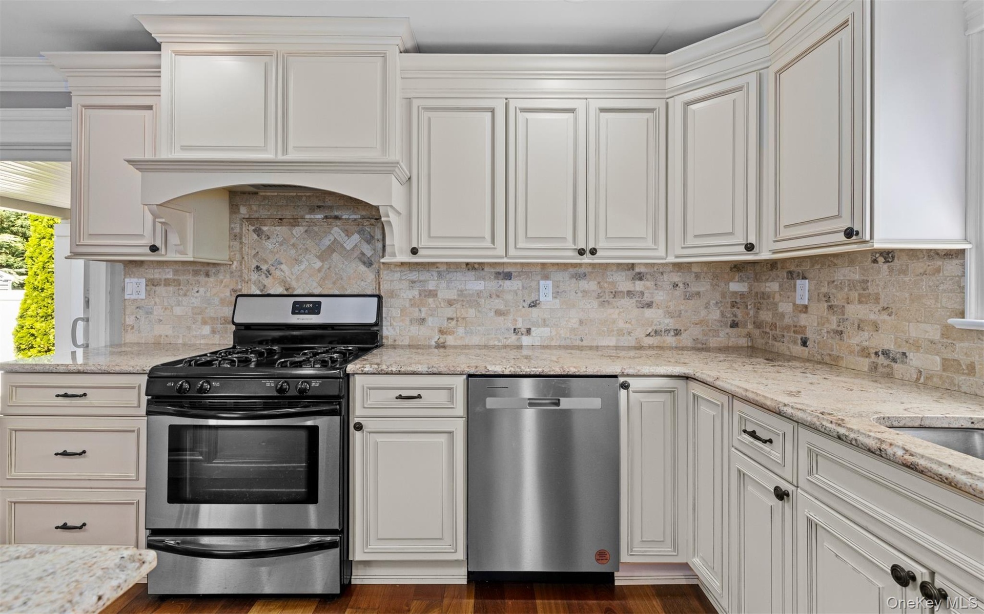 Cream-painted cabinetry, stone backsplash, stainless steel appliances, granite countertops, and wood-finish flooring