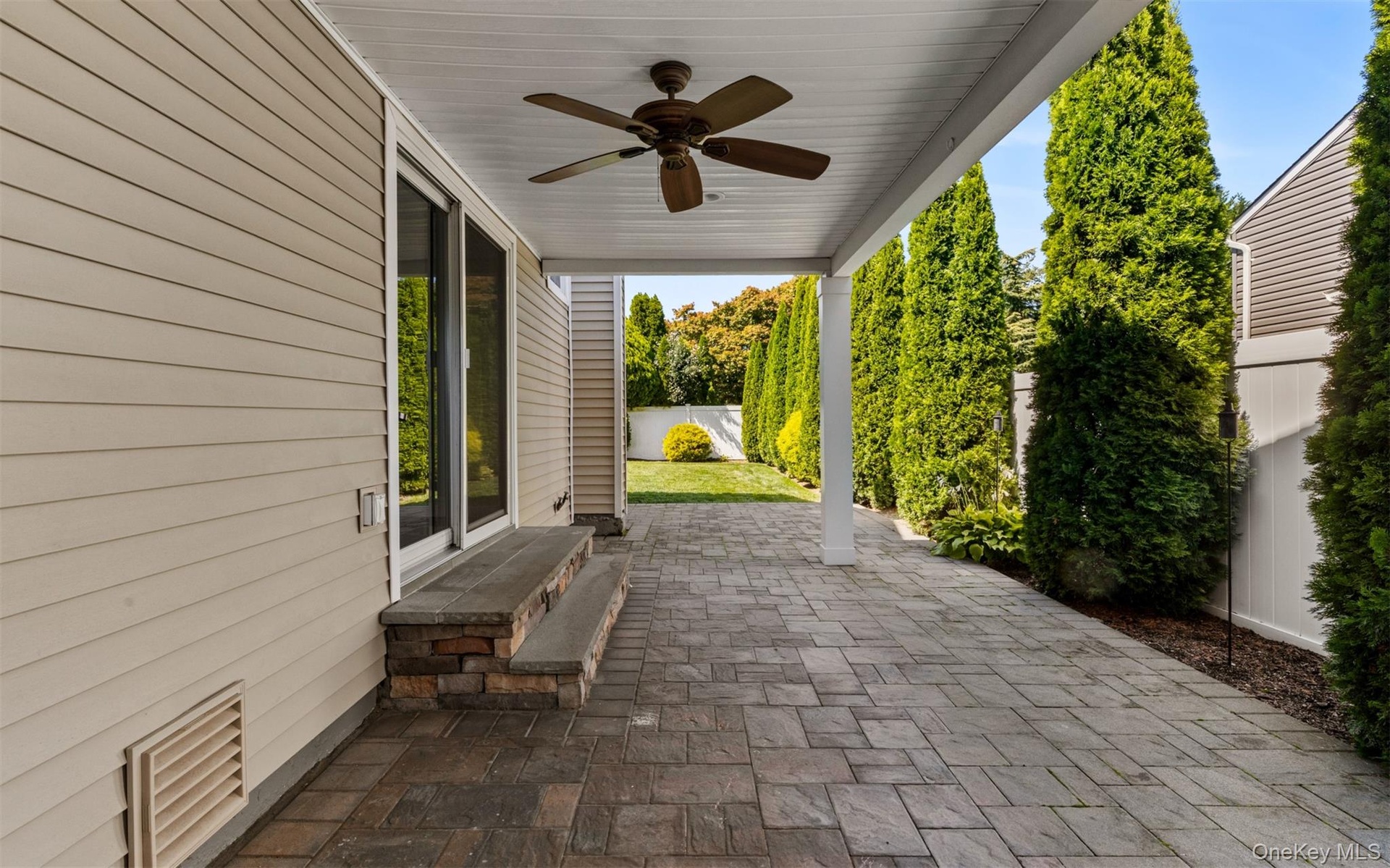 Covered patio featuring a ceiling fan, paver flooring, sliding glass doors, and privacy landscaping