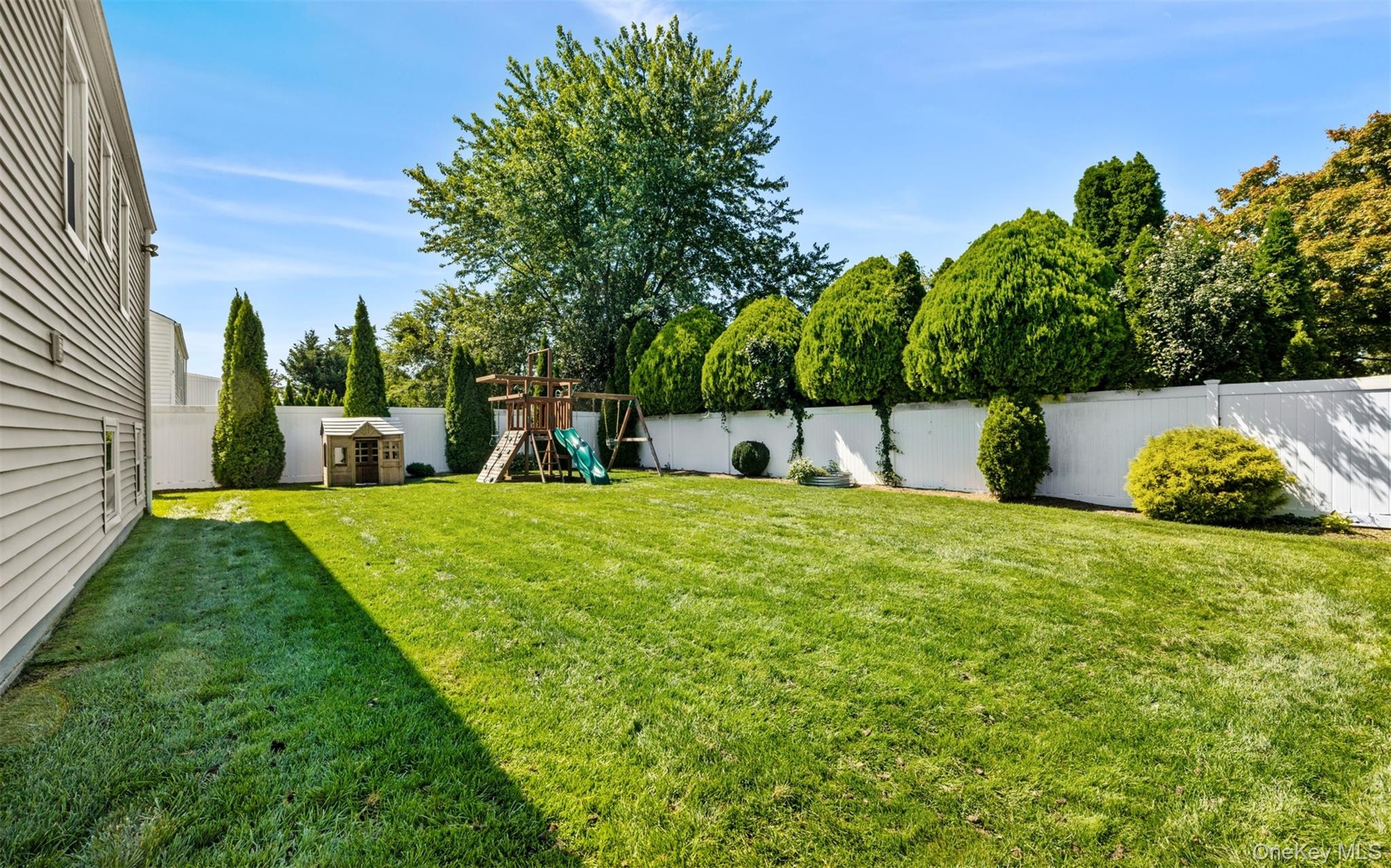 Expansive lawn area, white privacy fencing, and mature perimeter landscaping, fully fenced and In-ground speakers