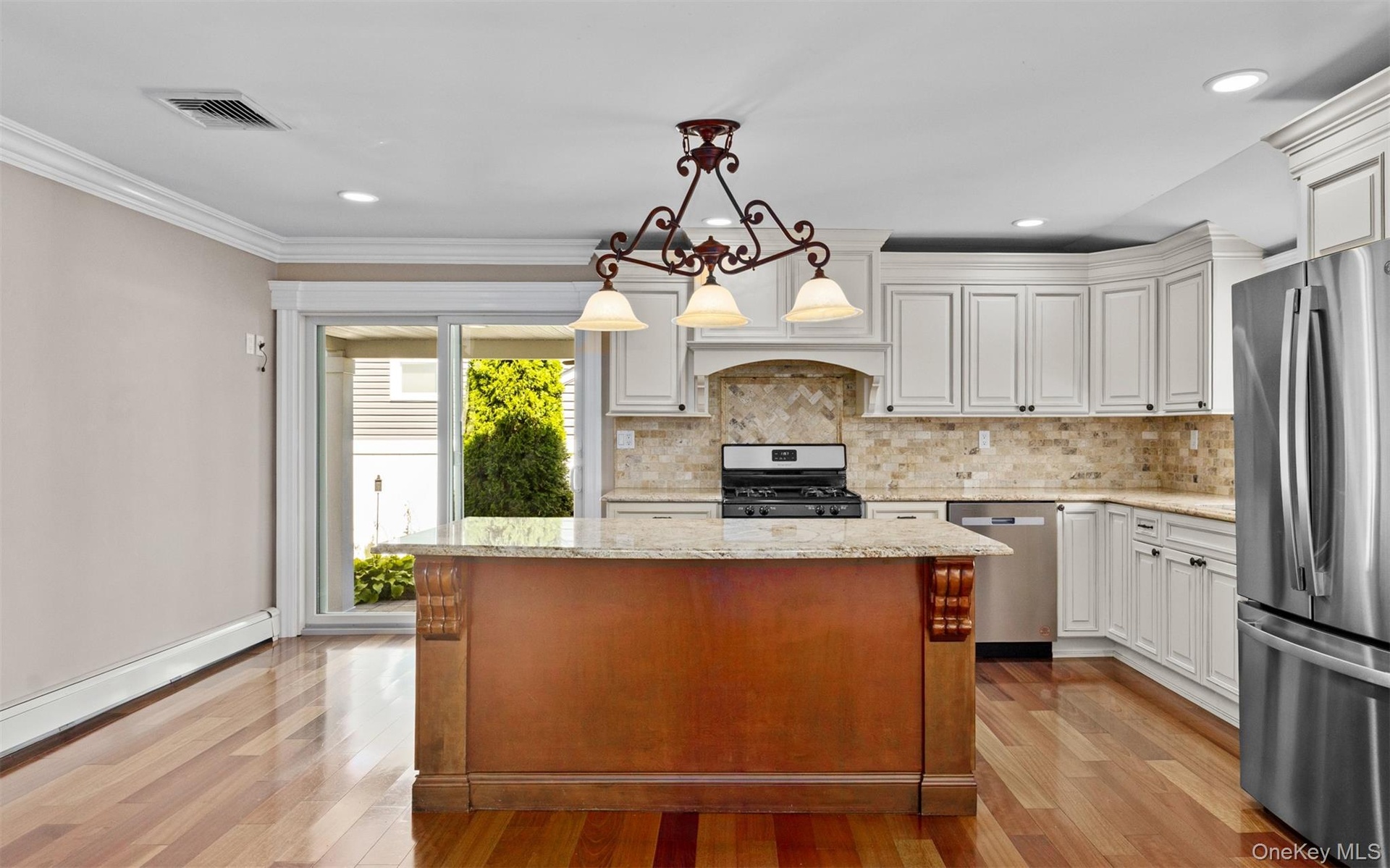 Kitchen featuring a central island with carved accents, stainless steel appliances, light-toned cabinetry, and wood-finish flooring