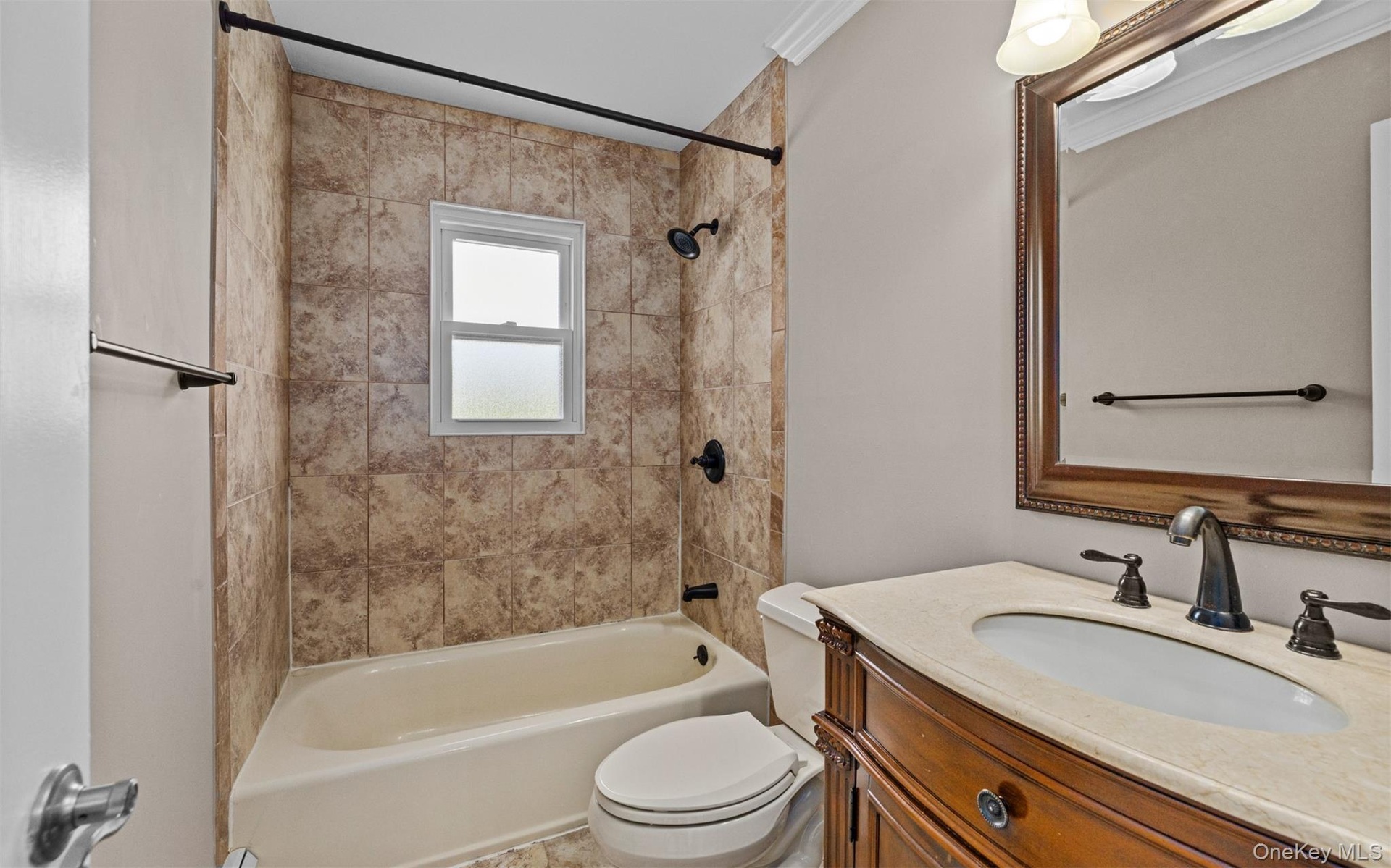 Bathroom featuring a bathtub with tile surround, shower, a built-in vanity with a stone countertop, a framed mirror, and crown molding