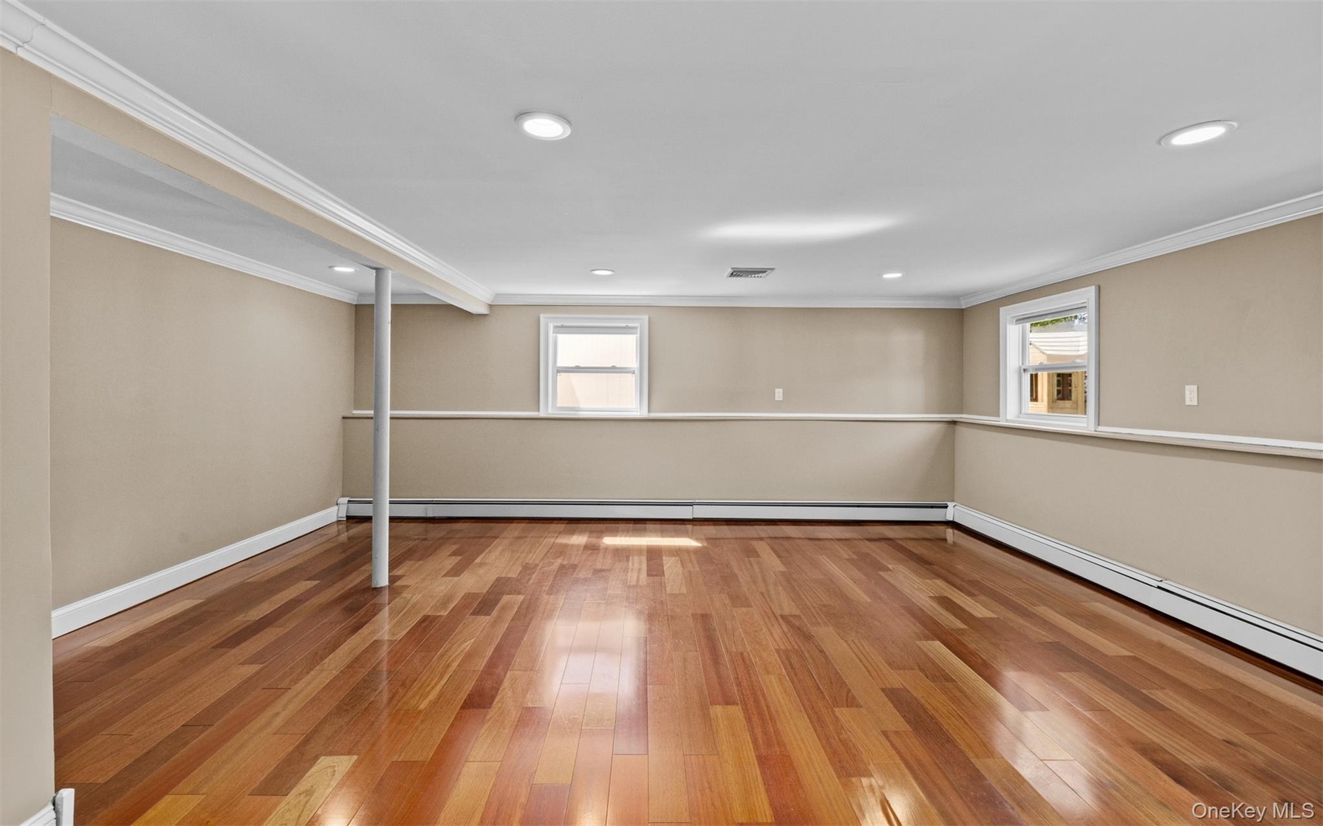 Cherry wood finish flooring, three windows with white trim, recessed lighting, crown molding, and chair rail detailing