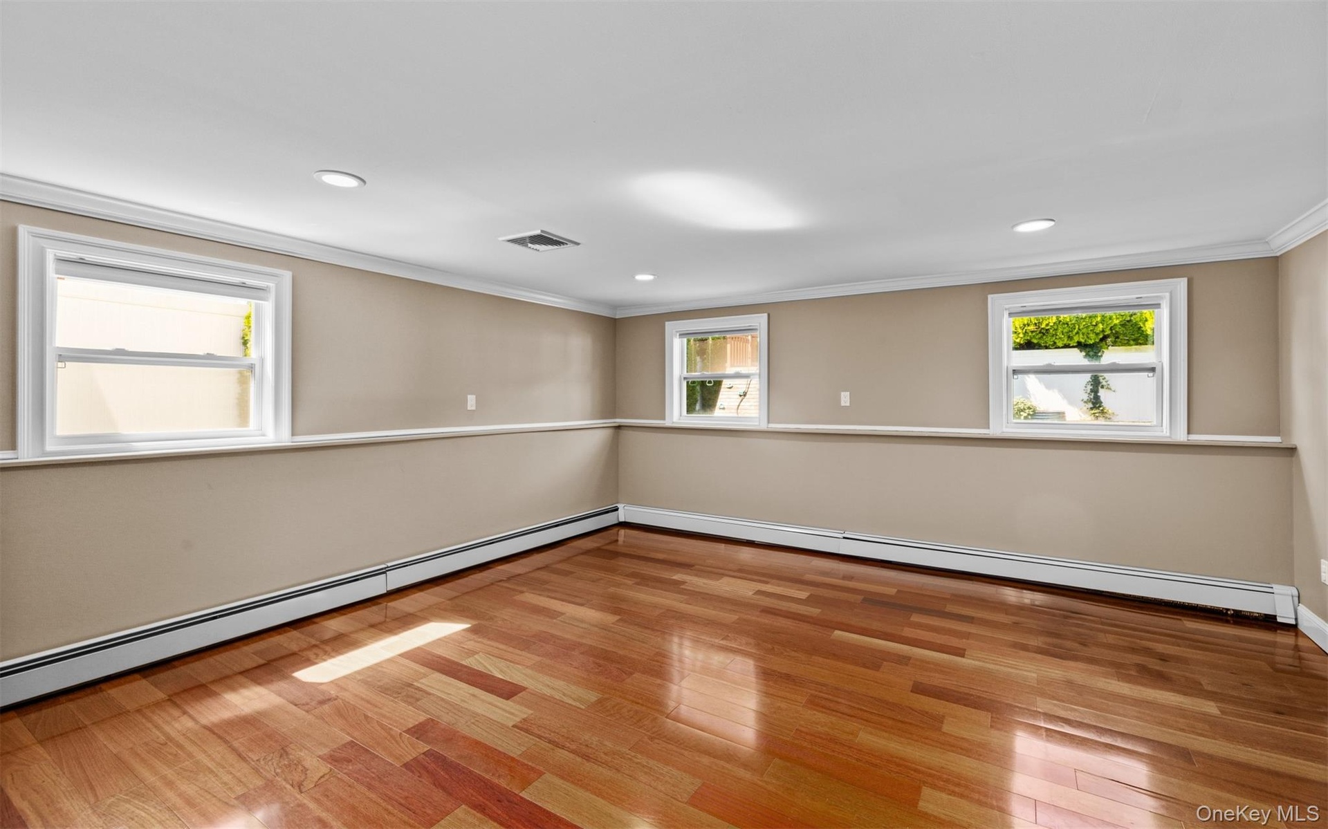 Cherry wood finish flooring, three windows with white trim, recessed lighting, crown molding, and chair rail detailing