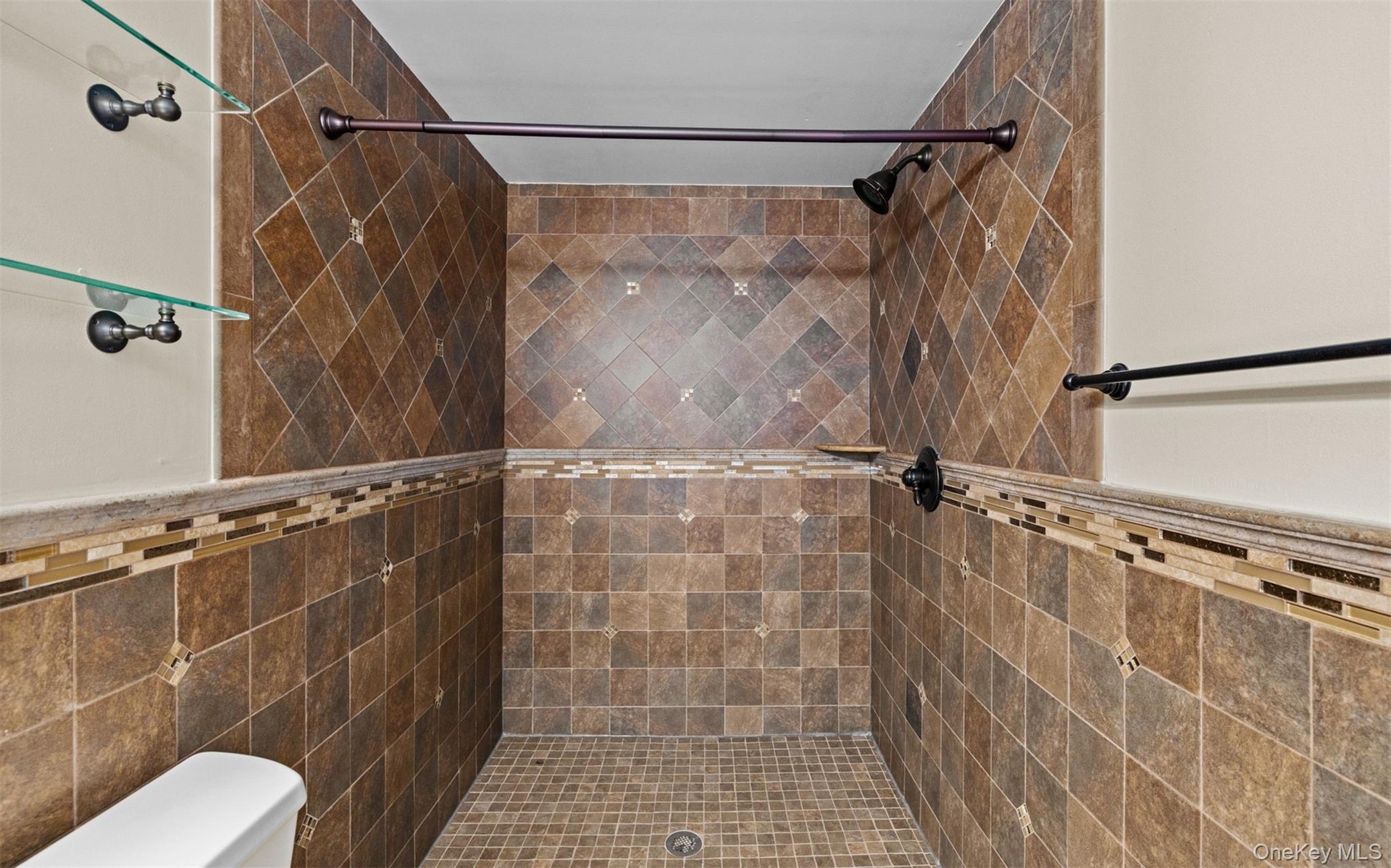 Tiled shower enclosure featuring a mosaic accent band, integrated showerhead, and glass shelving
