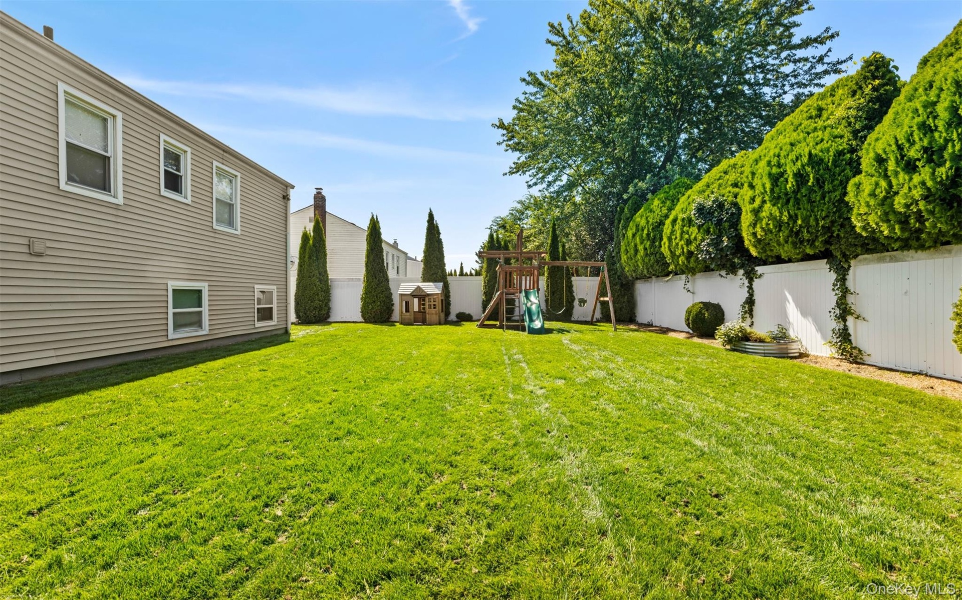 Expansive green lawn with a white privacy fence and mature perimeter plantings