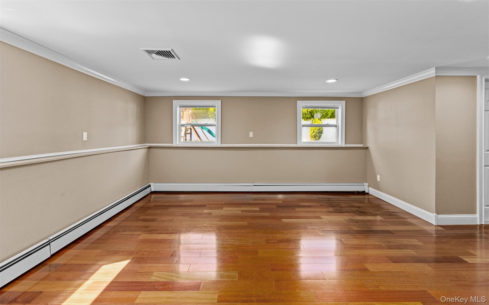 Cherry wood finish flooring, three windows with white trim, recessed lighting, crown molding, and chair rail detailing