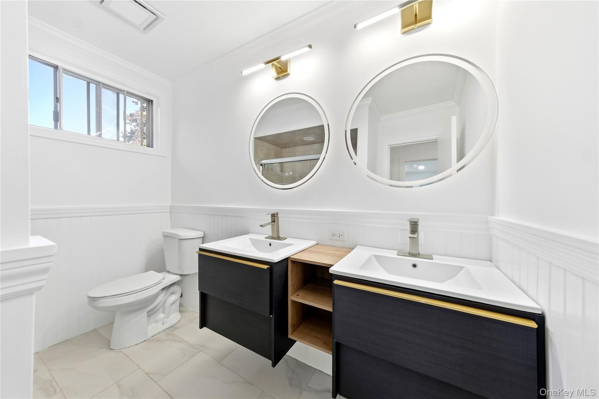 Dual floating vanities with integrated sinks, round back-lit mirrors, brushed gold fixtures and tub/shower combo