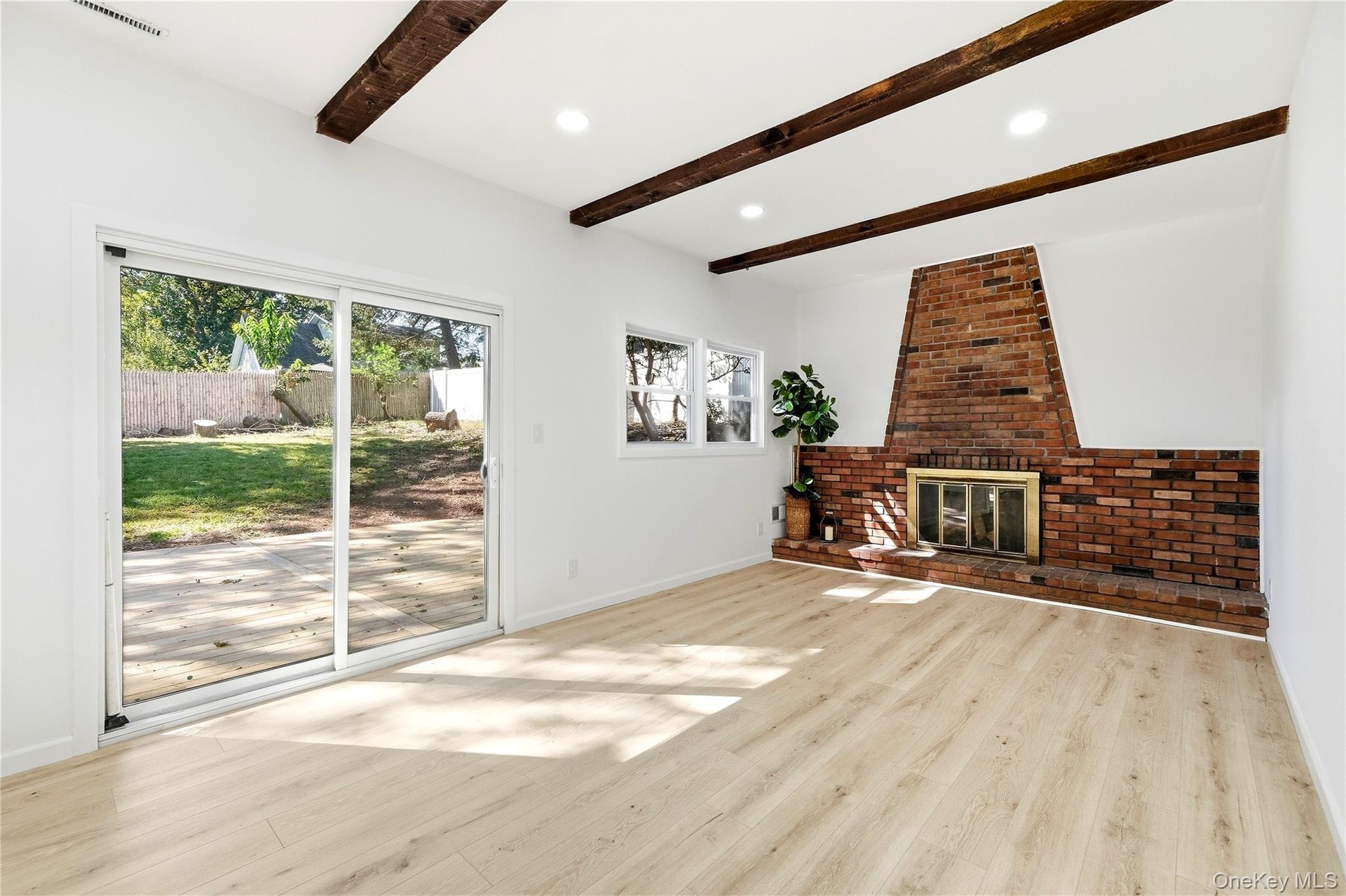 Wood-finish flooring, exposed ceiling beams, brick fireplace with metal insert, recessed lighting, and sliding glass door to a private outdoor space