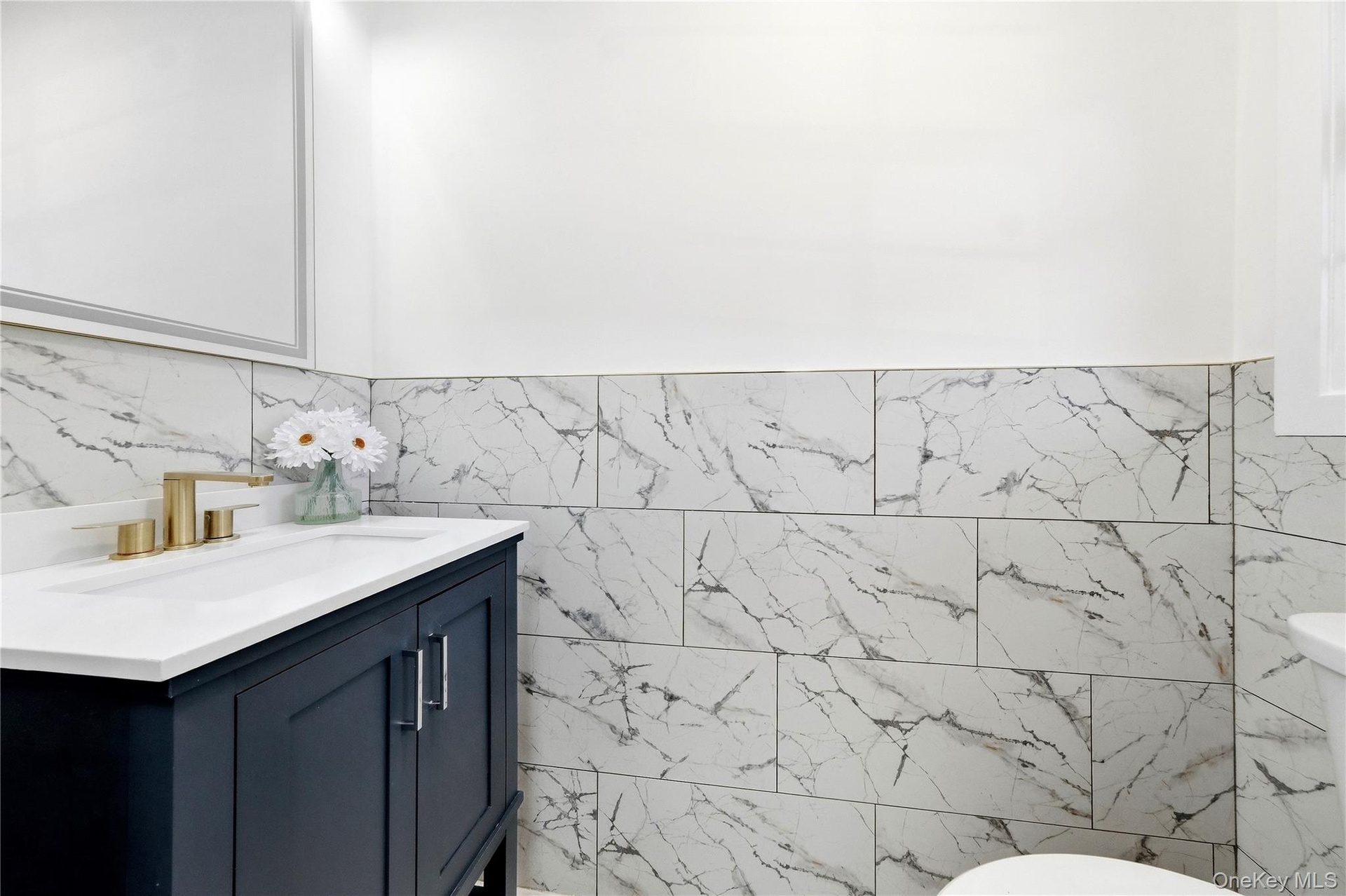 Dark-toned vanity with brushed gold-finish hardware, a white countertop, and an integrated rectangular sink and toilet.