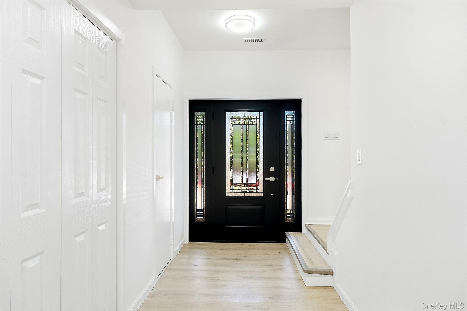 Black entry door with decorative glass side panels, wood-finish flooring, two white paneled closet doors, and a half bathroom
