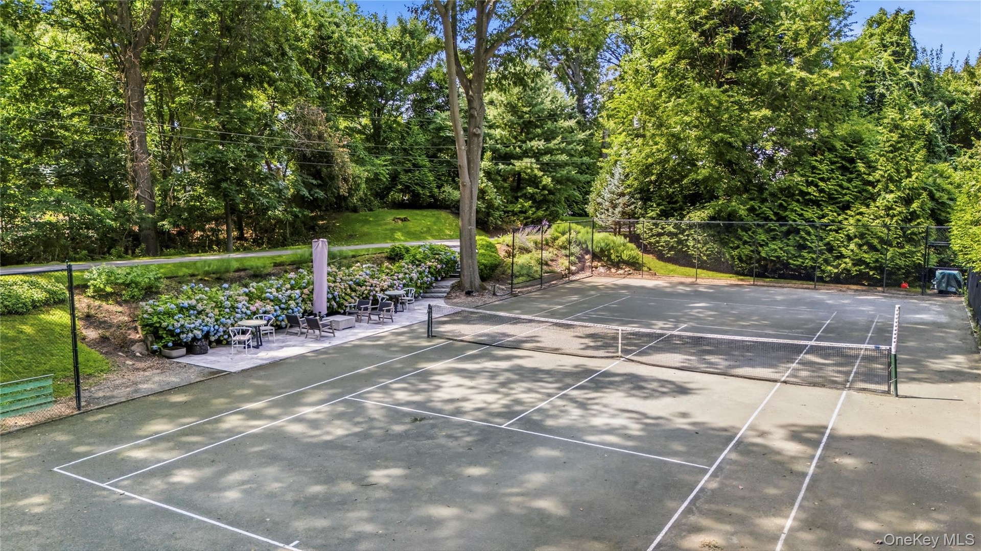 Private tennis court with surrounding mature trees and landscaping