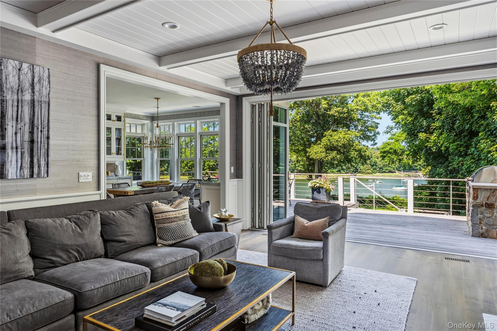 Expansive living area with gas fireplace opening to a large outdoor deck with a stone-clad built-in grill and cable railing